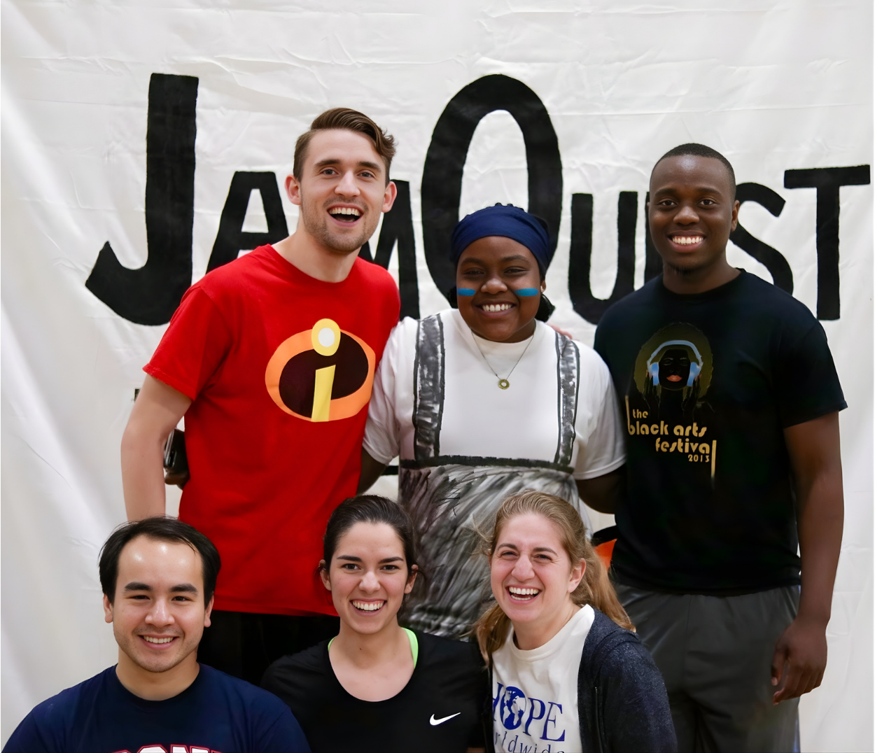 Group of six diverse young adults smiling in front of a white banner with black text that reads 'JAM OUST'.