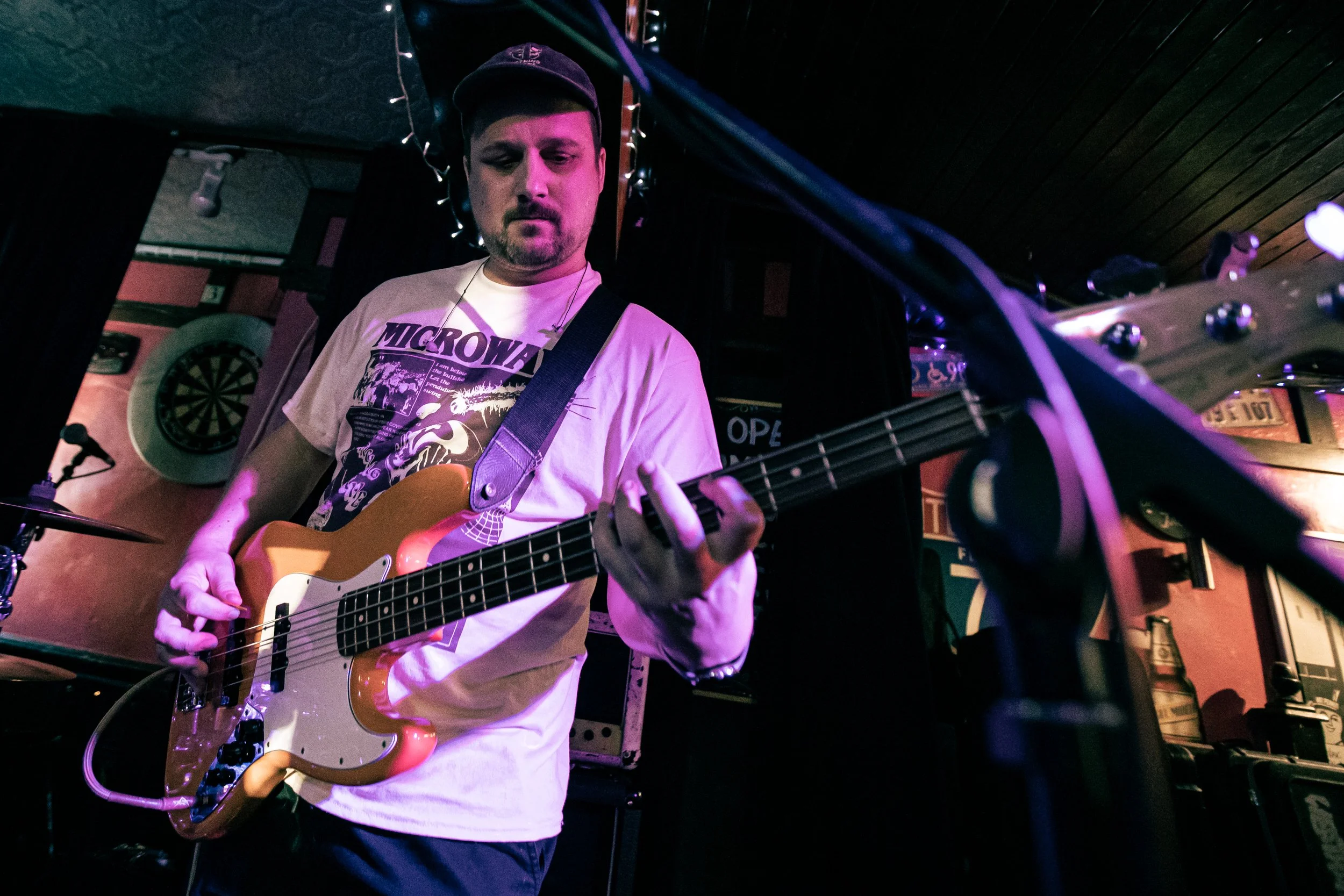 A man playing bass guitar on stage in a dimly lit venue with decorations and lighting effects.