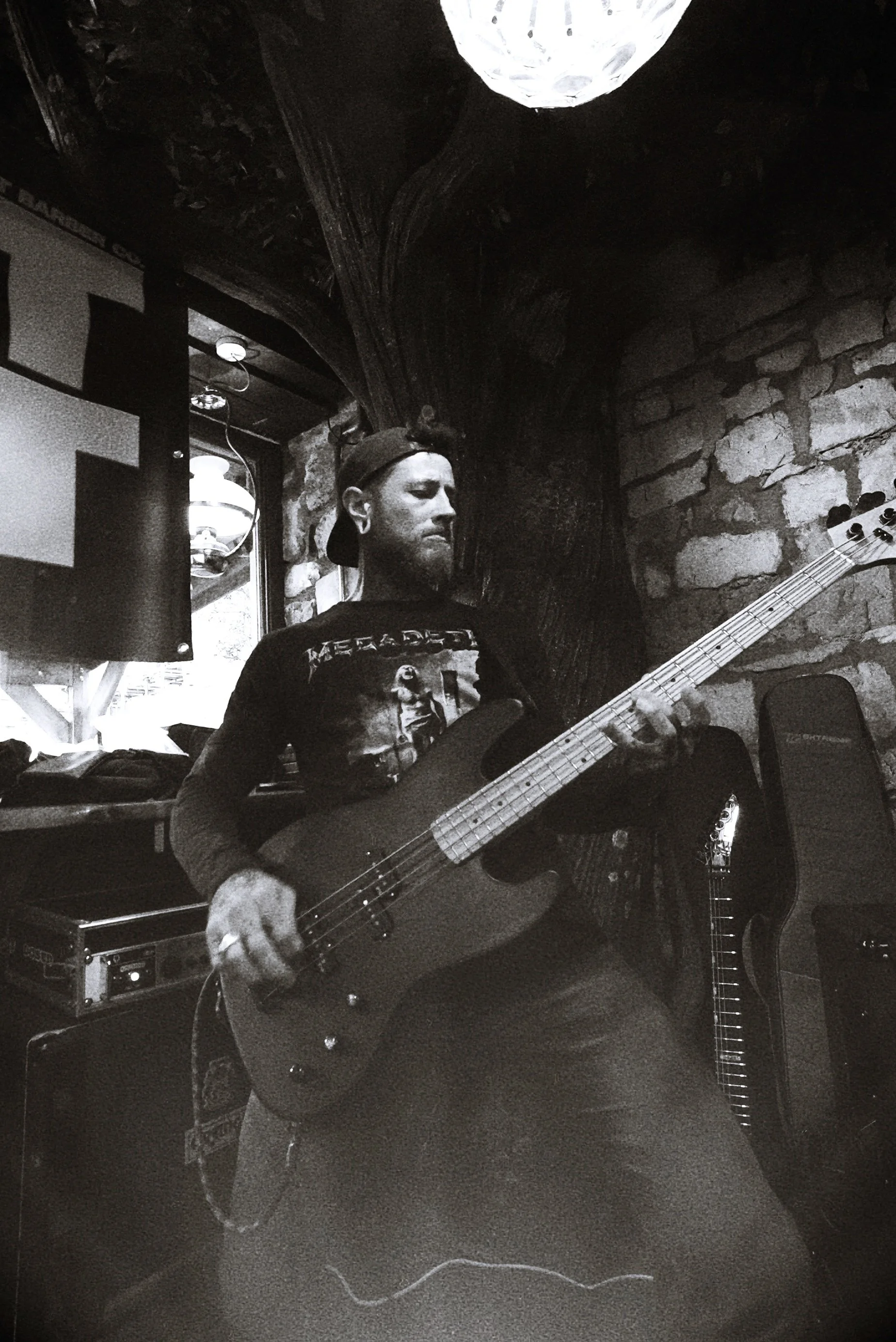 A man playing an electric bass guitar in a dimly lit room with brick walls and decorative elements.