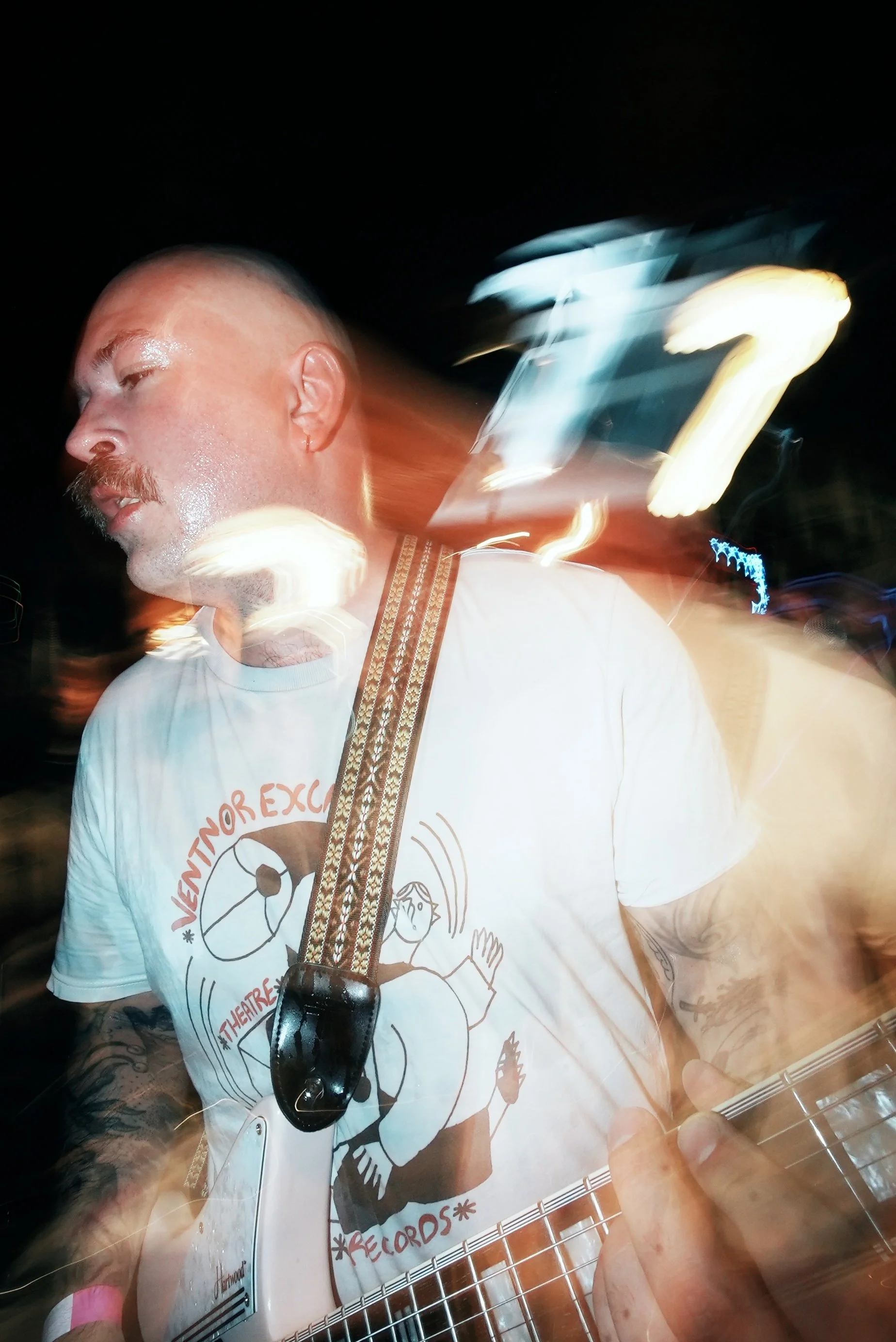 A man playing electric guitar at night with motion blur and light trails.