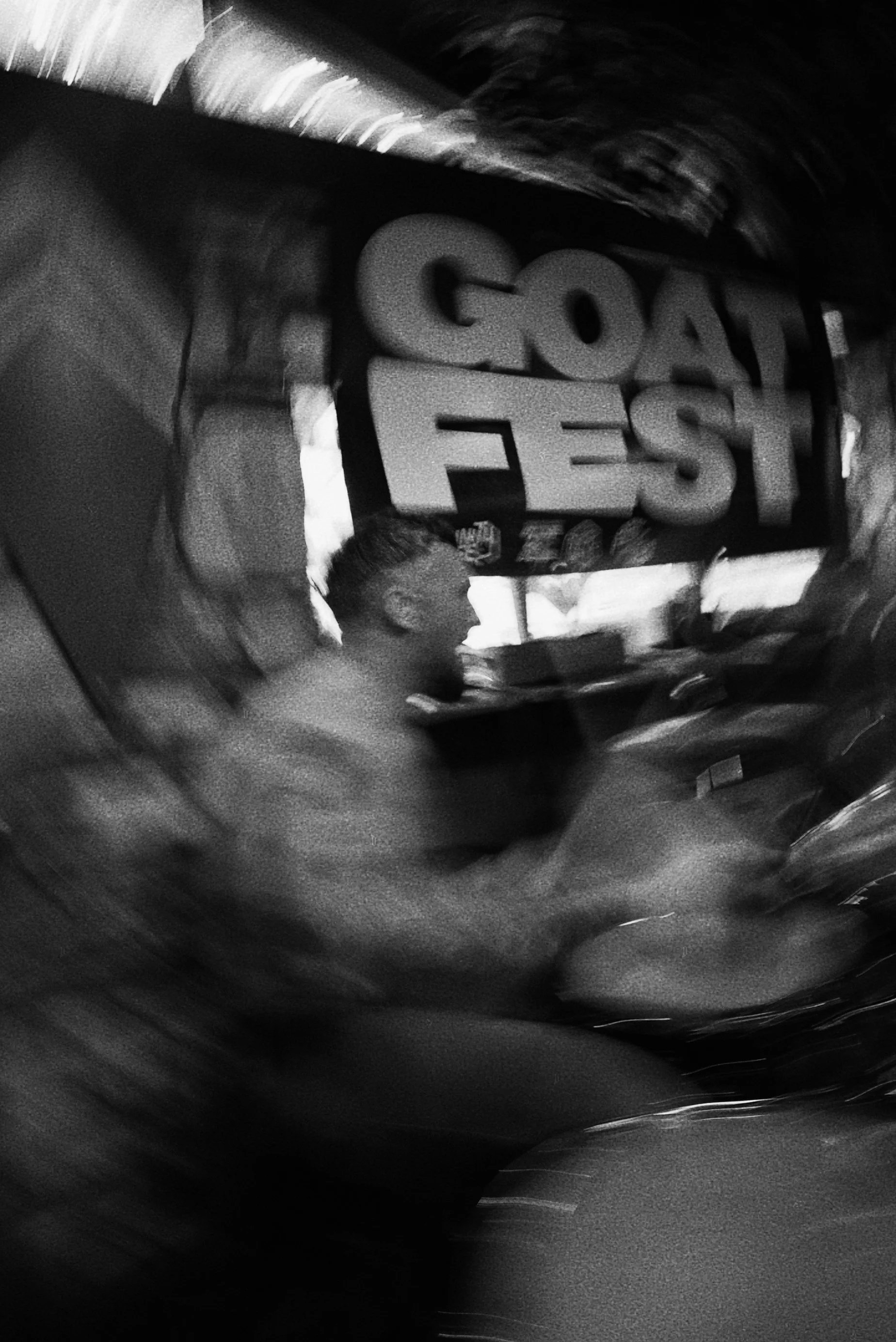 A blurred black-and-white photo of a person sitting at a table with a large sign reading 'GREAT FEST' in the background.