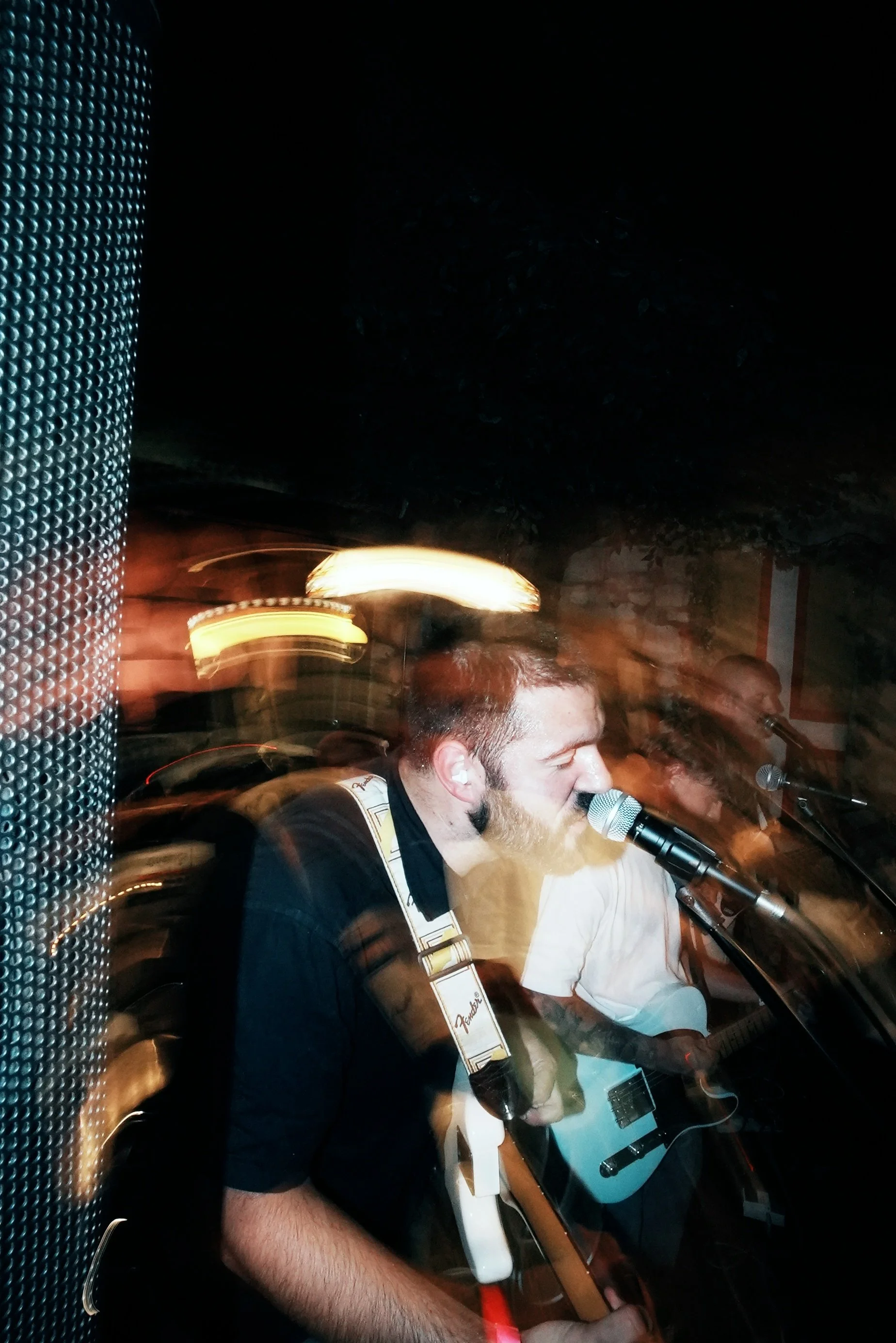 A musician singing into a microphone while playing an electric guitar, with motion blur effects in a dimly lit environment.