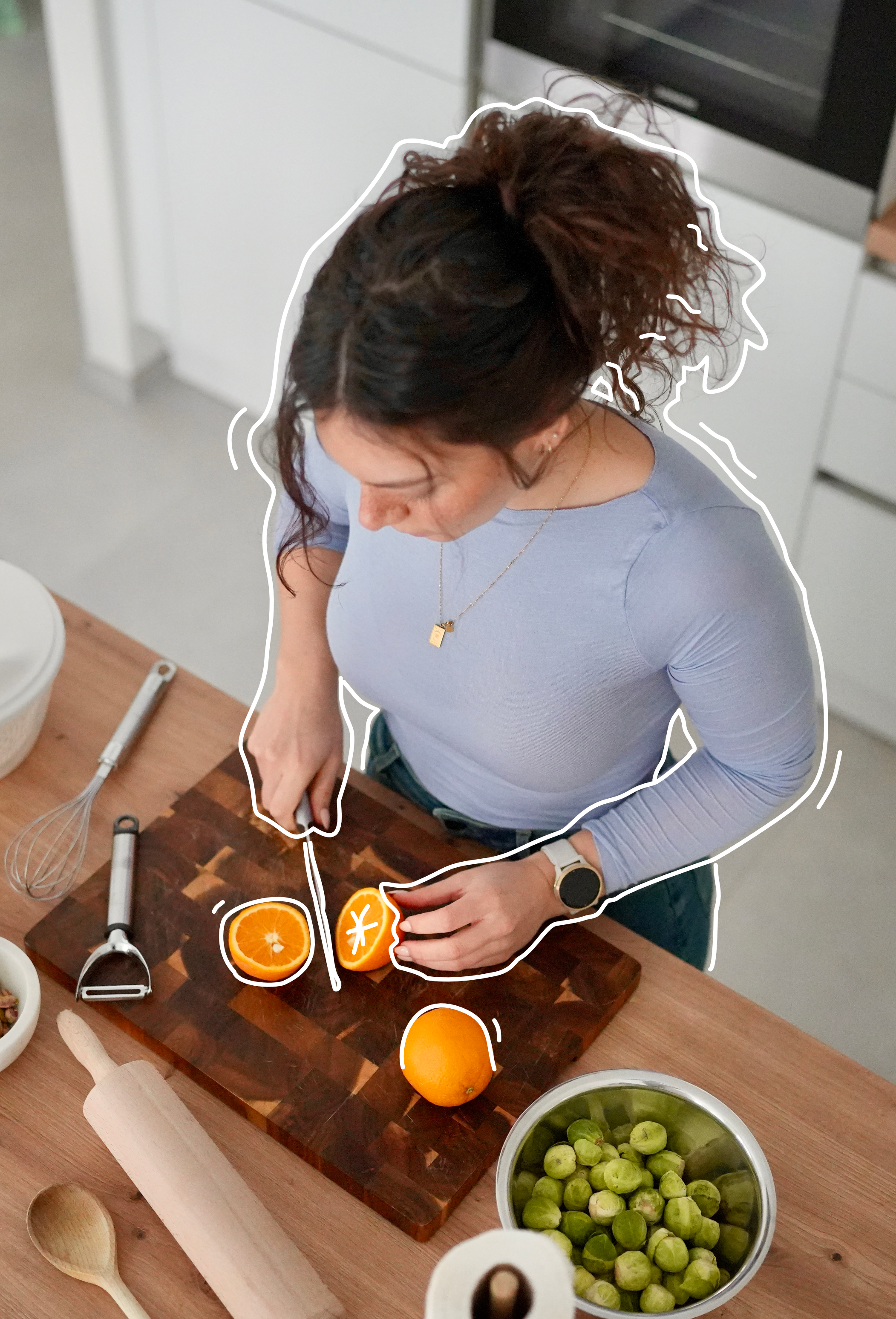 Une femme coupe une orange à l'aide d'un couteau sur une planche en bois dans une cuisine.