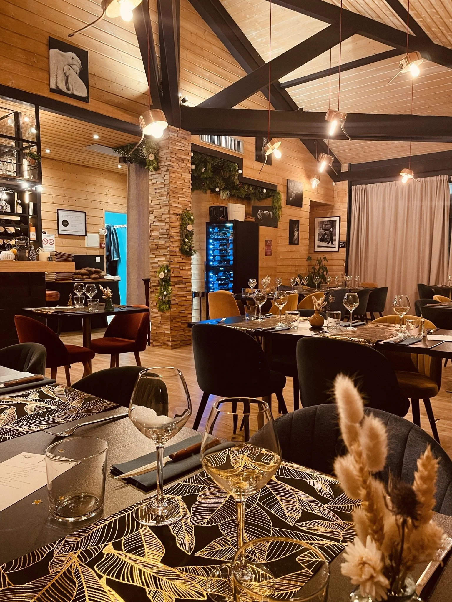 Salle du restaurant Alexpérience avec tables décorées, verres à vin, assiettes, et un éclairage chaleureux. Décor en bois, avec des peintures d'artistes. La pièce est élégamment dressée pour un dîner.