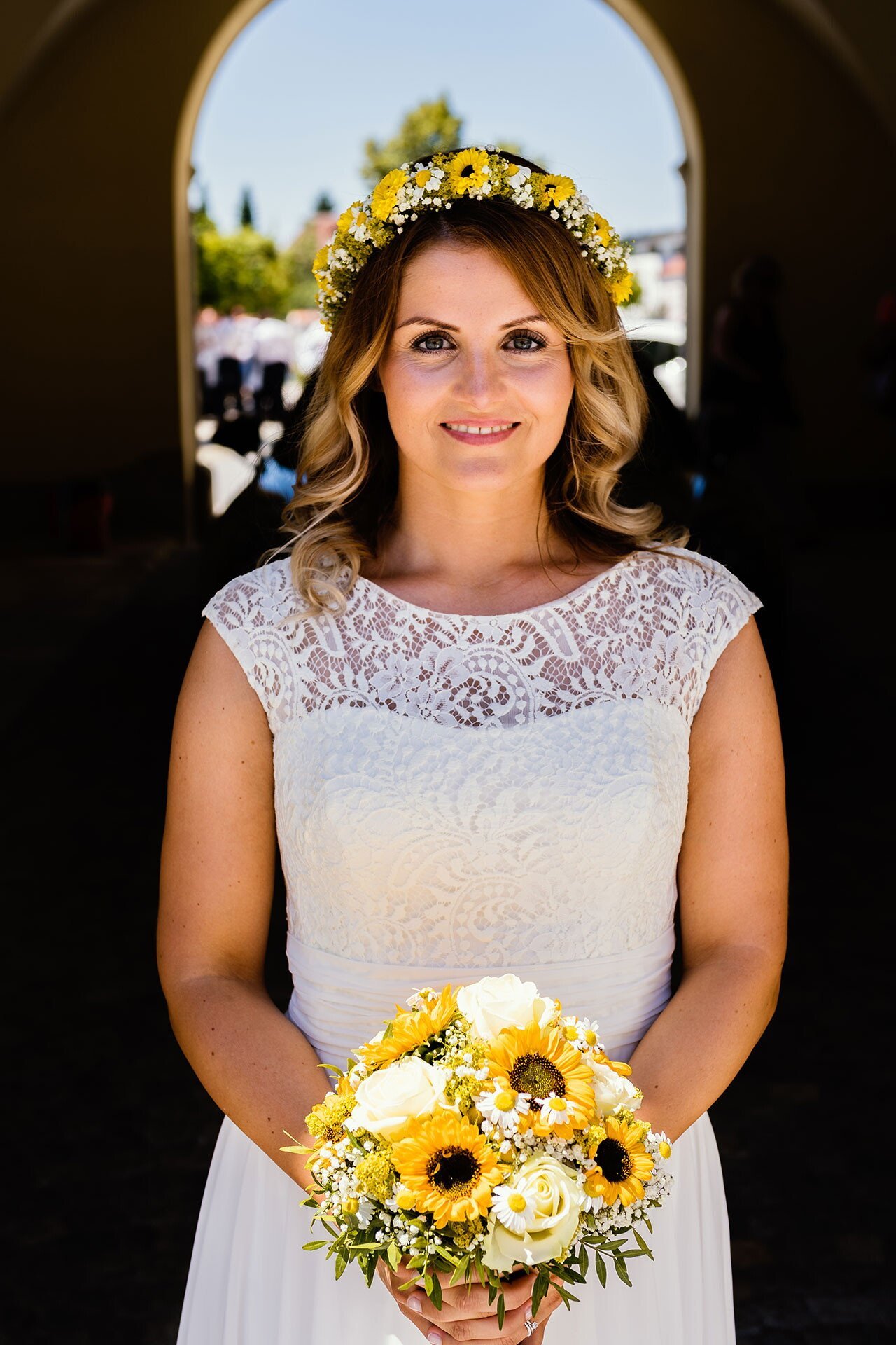 Braut mit Blumenkranz und Blumenstrauß vor dunklem Hintergrund bei einer Hochzeit.