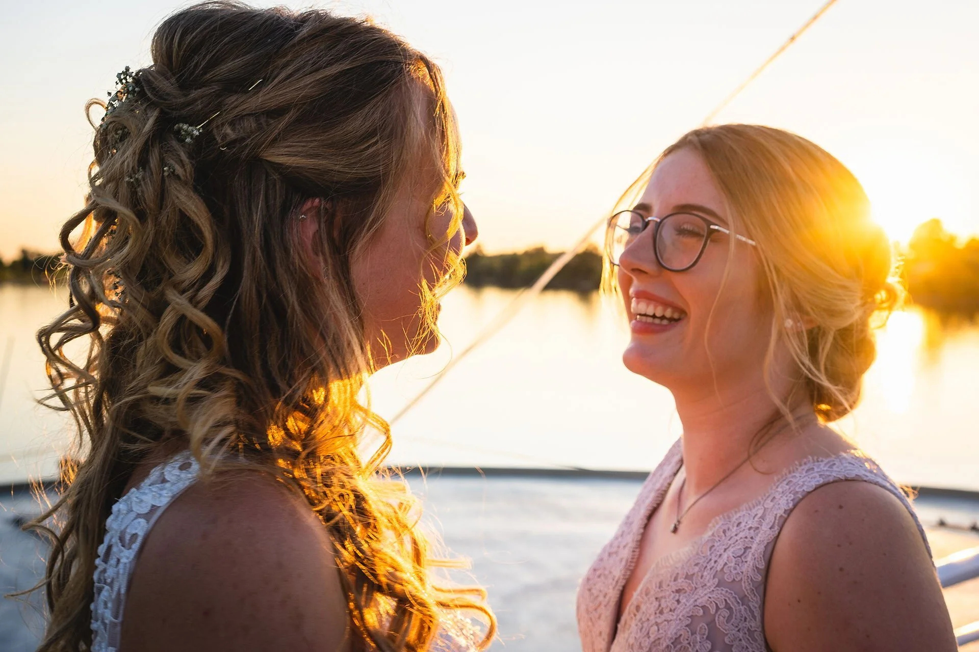 Zwei Frauen feiern auf einem Boot bei Sonnenuntergang und lachen miteinander.