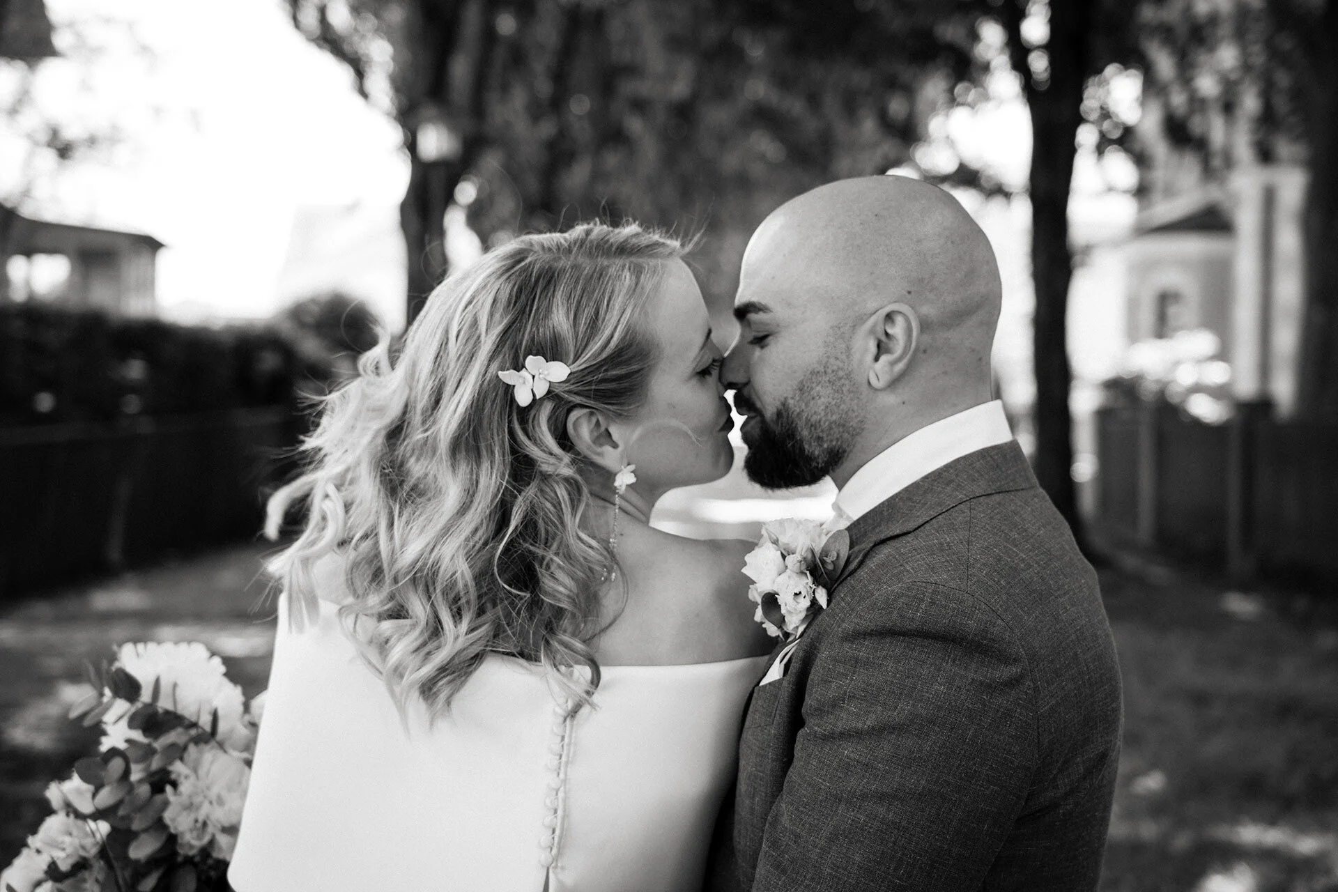 Ein Brautpaar bei einer Hochzeit, das sich küsst, draußen im Park, schwarz-weiß Fotografie.