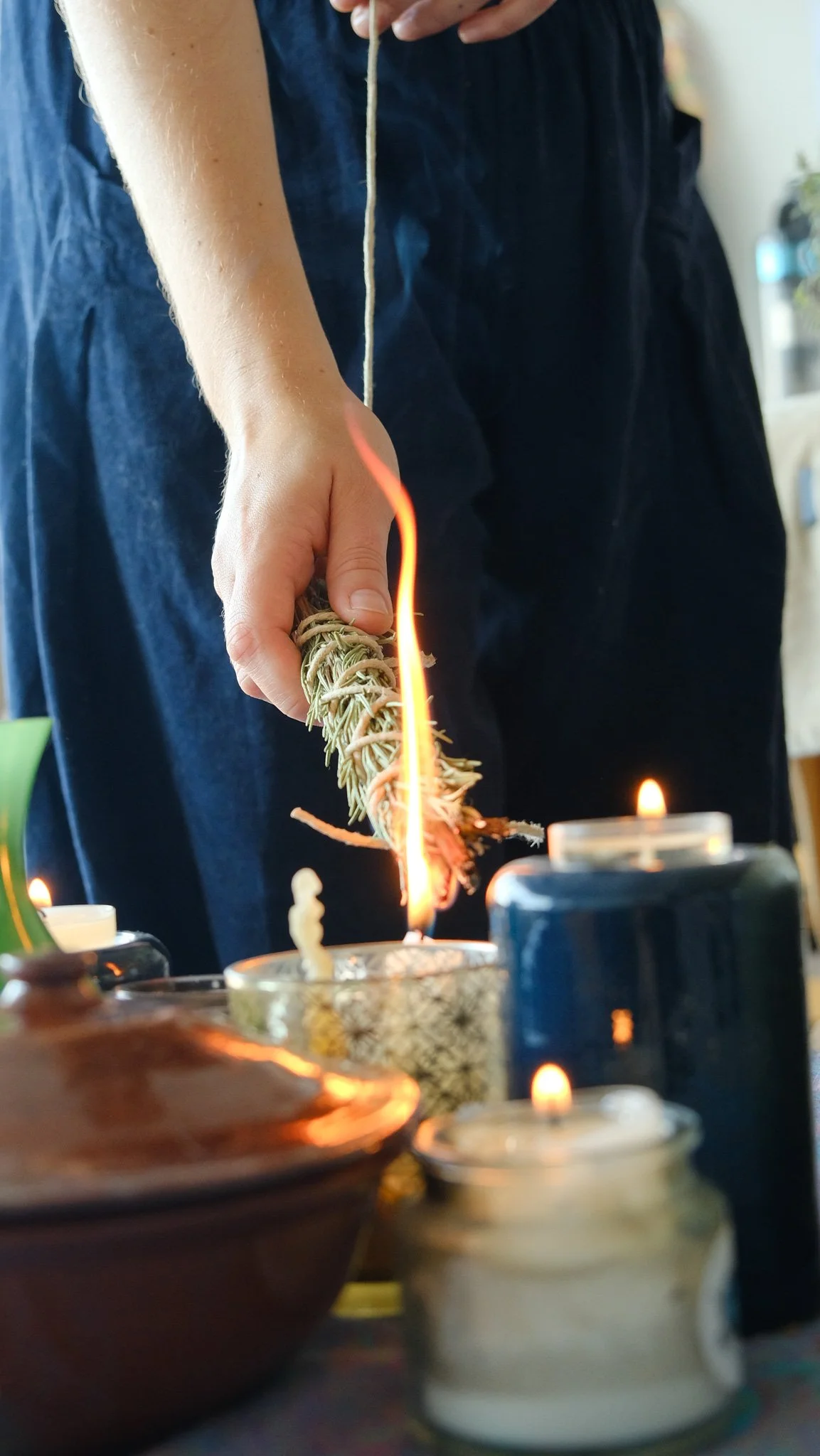 Une personne tient une branche de romarin enflammée, entourée de bougies allumées sur une table.