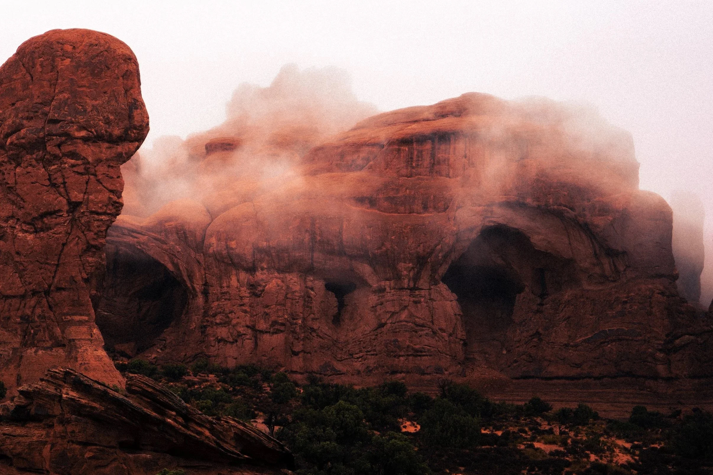 Red rock formations with caves, partially obscured by mist and fog in Moab, Utah.