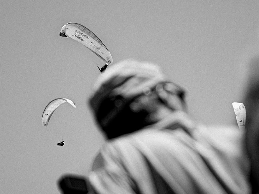 Red Bull X-Alps Paragliders flying in the sky with a person in the foreground watching them.
