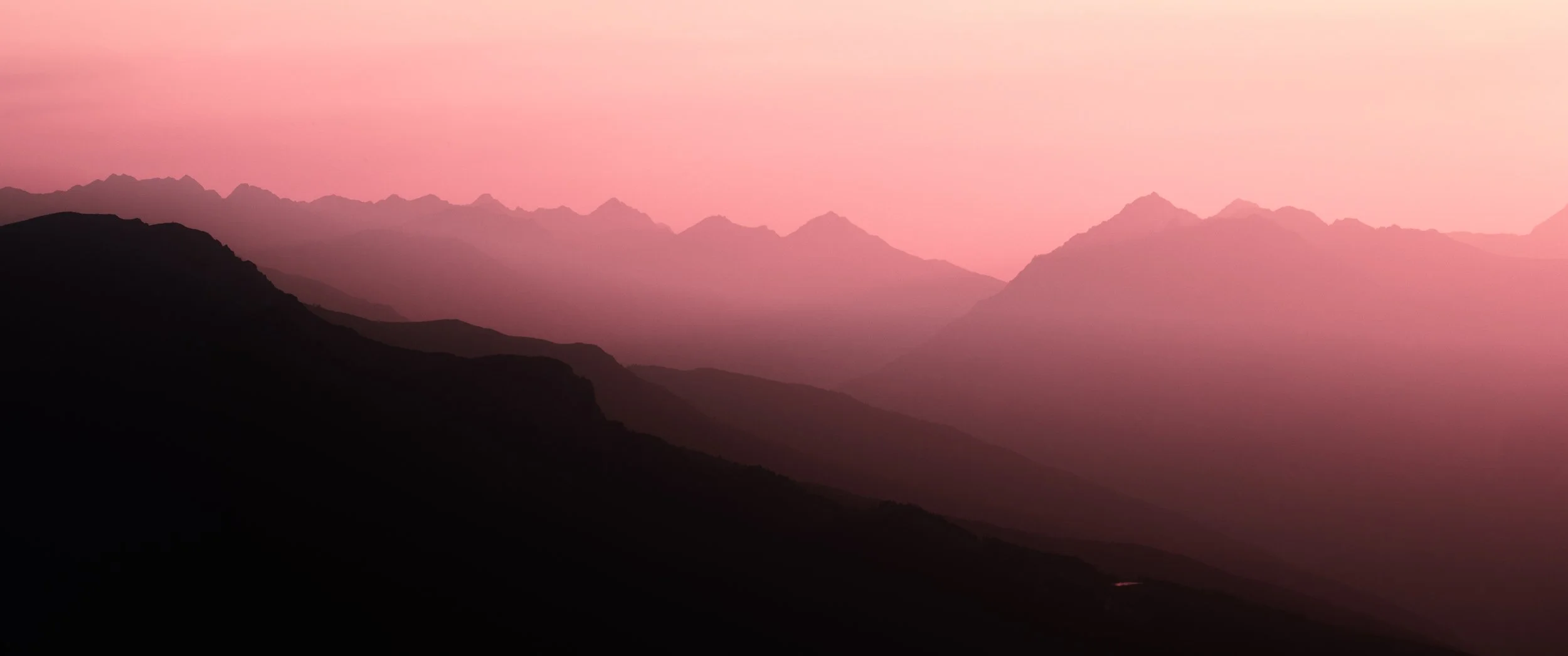 Silhouetted mountain range during pinkish sunset or sunrise with layered peaks fading into the distance on Patscherkofel, in Innsbruck, Tirol, Austria.