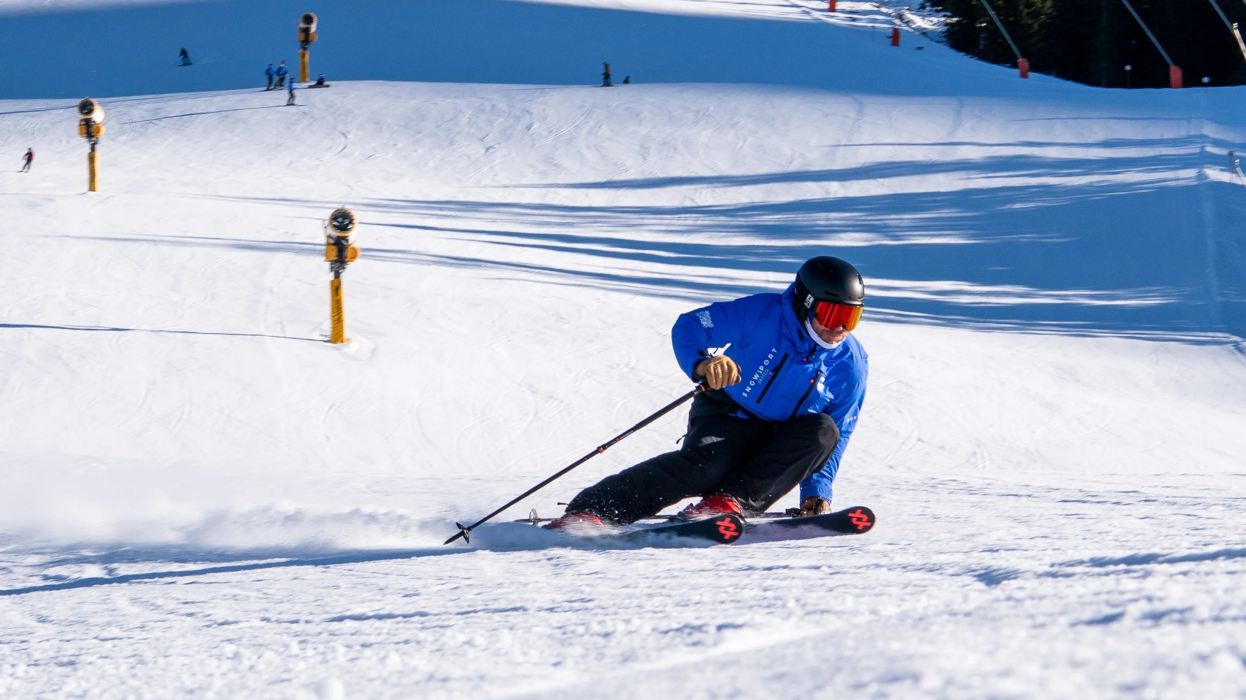A skier in a blue jacket and black pants speeding down a snowy slope in a ski resort with a blue sky and mountain in the background in Seefeld in Tirol, Austria.