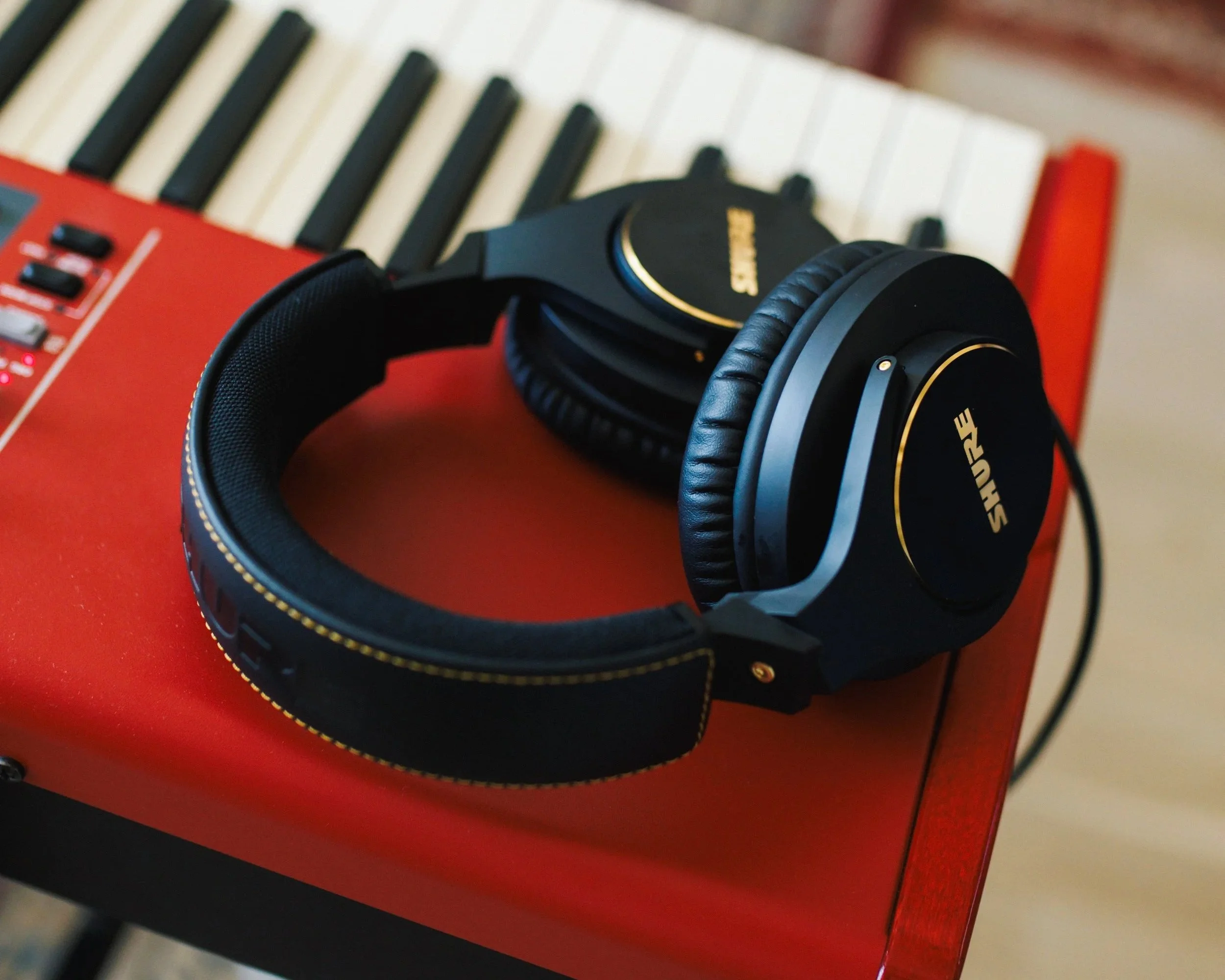 Black Shure headphones resting on a red keyboard or synthesizer with black and white keys.