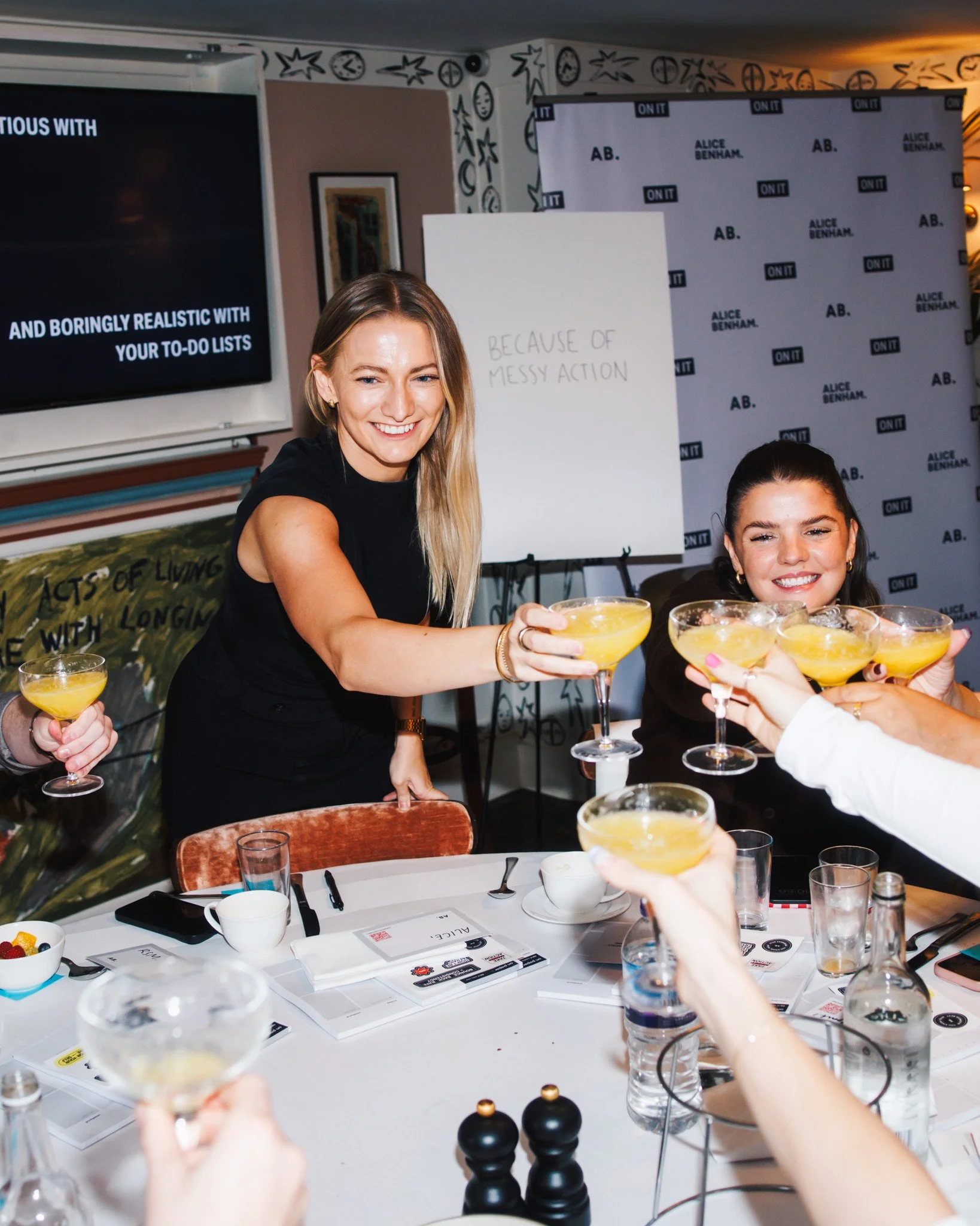 Group of people raising glasses for a toast in a meeting room with a woman smiling at the camera.