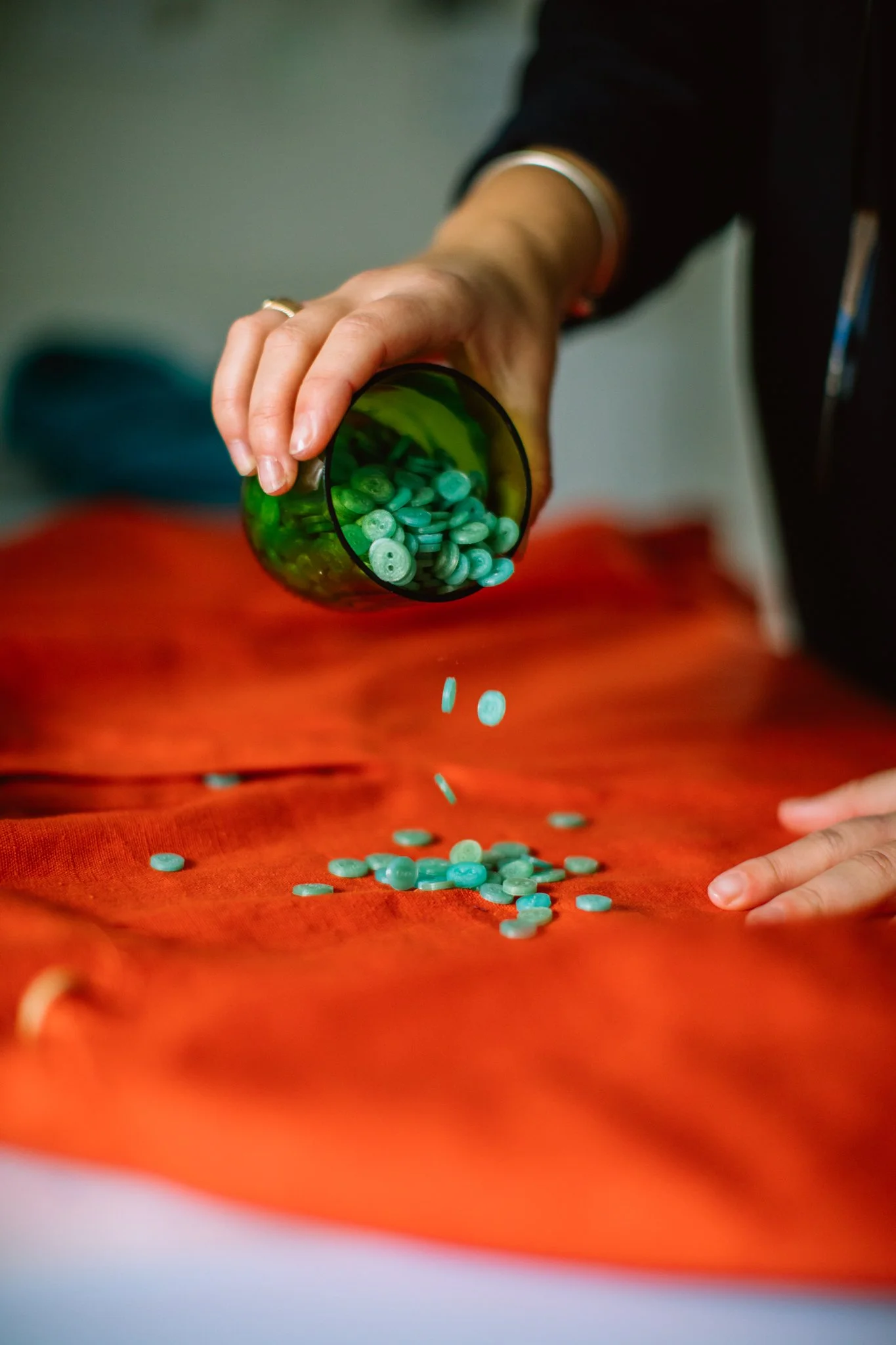 Person pouring green pills from a green container onto a red cloth surface.