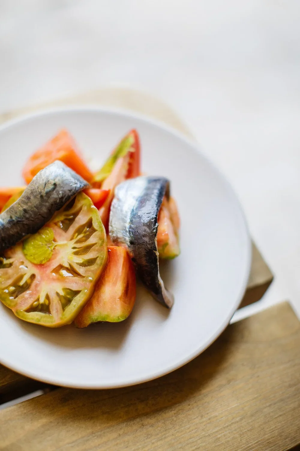 Close-up of a white bowl of mixed tomatoes and sardines on a wooden surface.