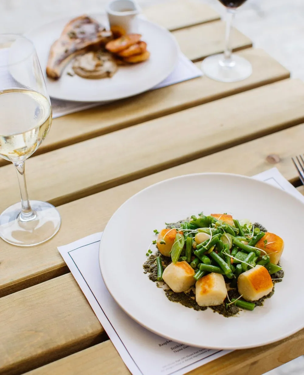 Plate with green beans, carrots, and scallions, garnished with microgreens on a white plate, with a glass of white wine nearby and a wooden table.