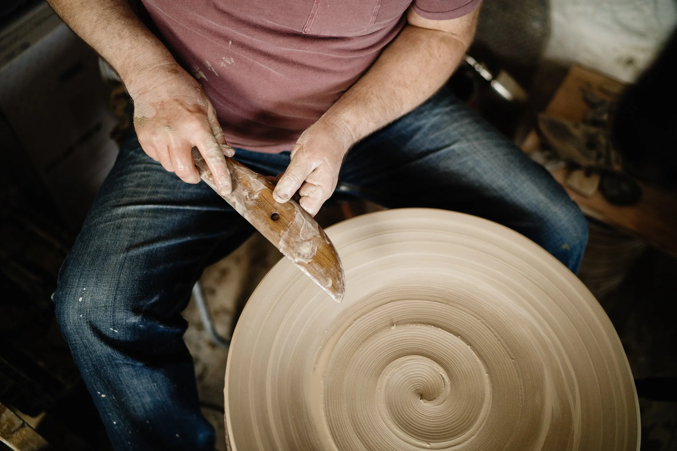 A person shaping a ceramic piece on a pottery wheel in a workshop, with a focus on their hands and the spinning clay.