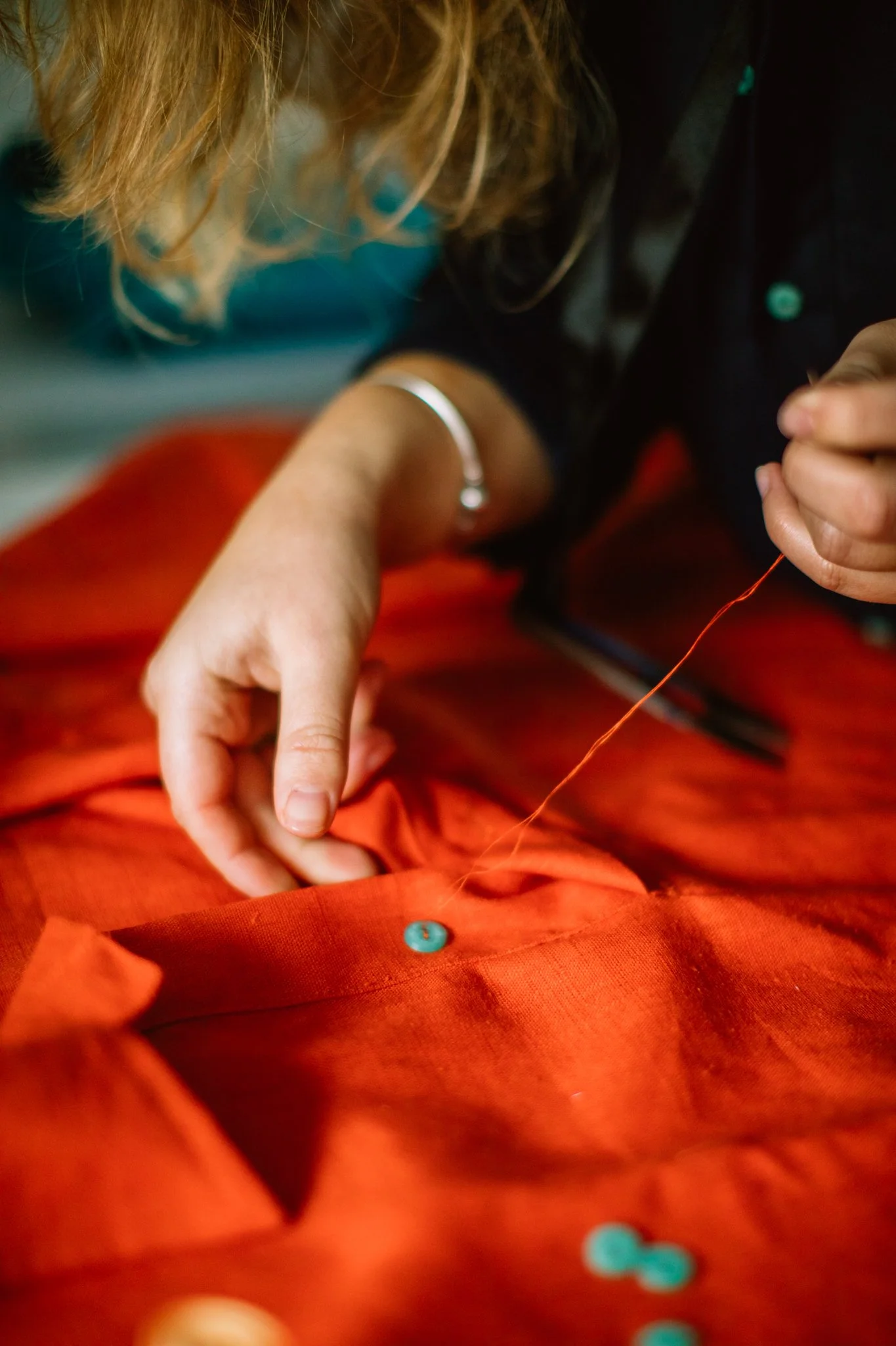 A person sewing orange fabric using a needle and thread, with buttons sewn onto the fabric.
