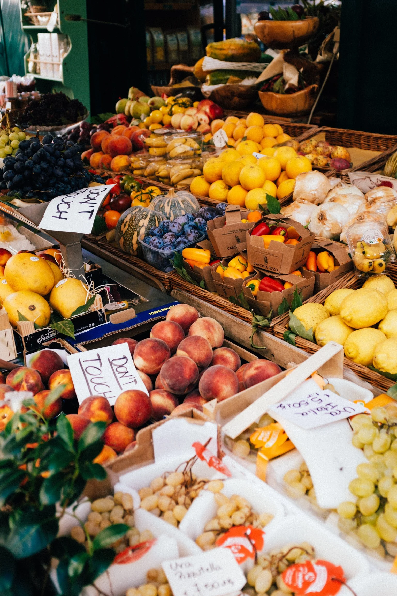 Display of fresh fruits and vegetables at a market stand, including peaches, grapes, lemons, garlic, and peppers.