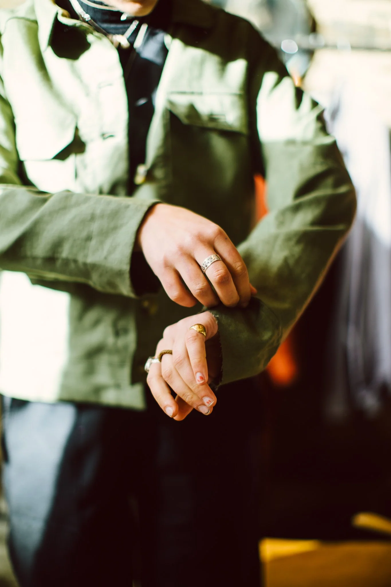 Close-up of a person adjusting their green jacket sleeve, showing multiple rings on their fingers.