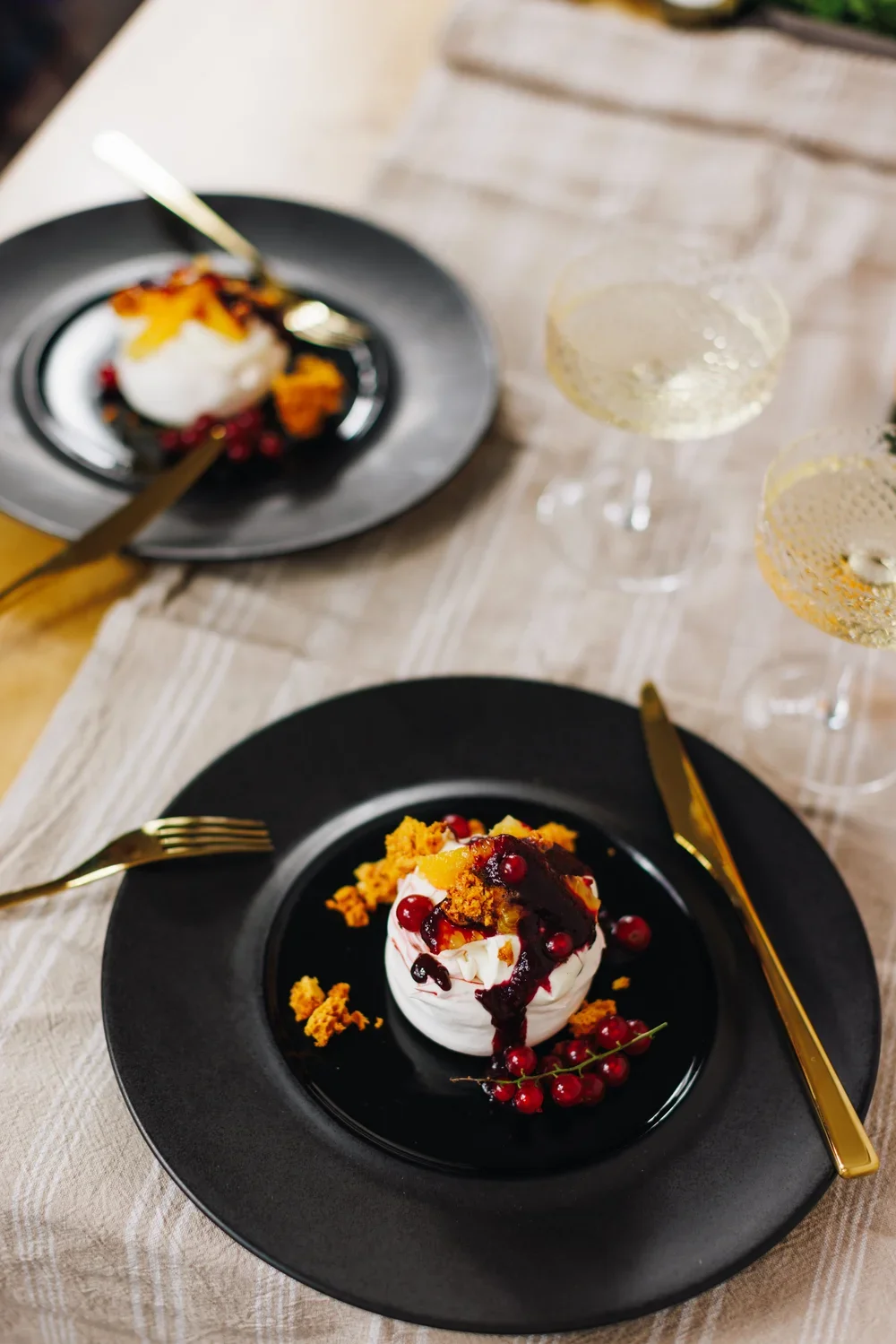 A dessert with white cream, red berries, and sauce on a black plate.
