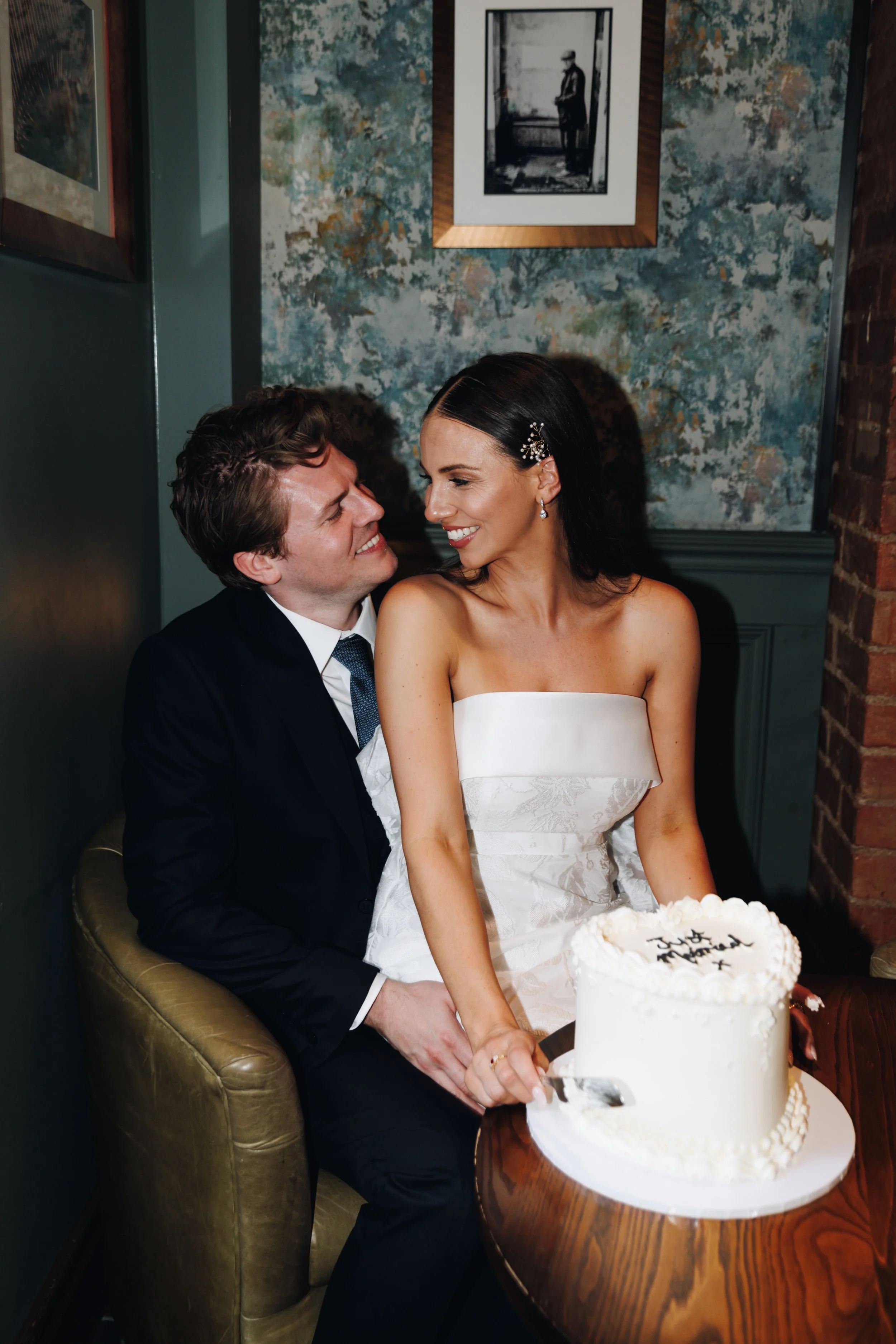 Couple at a wedding celebration with a white wedding cake on a wooden table.