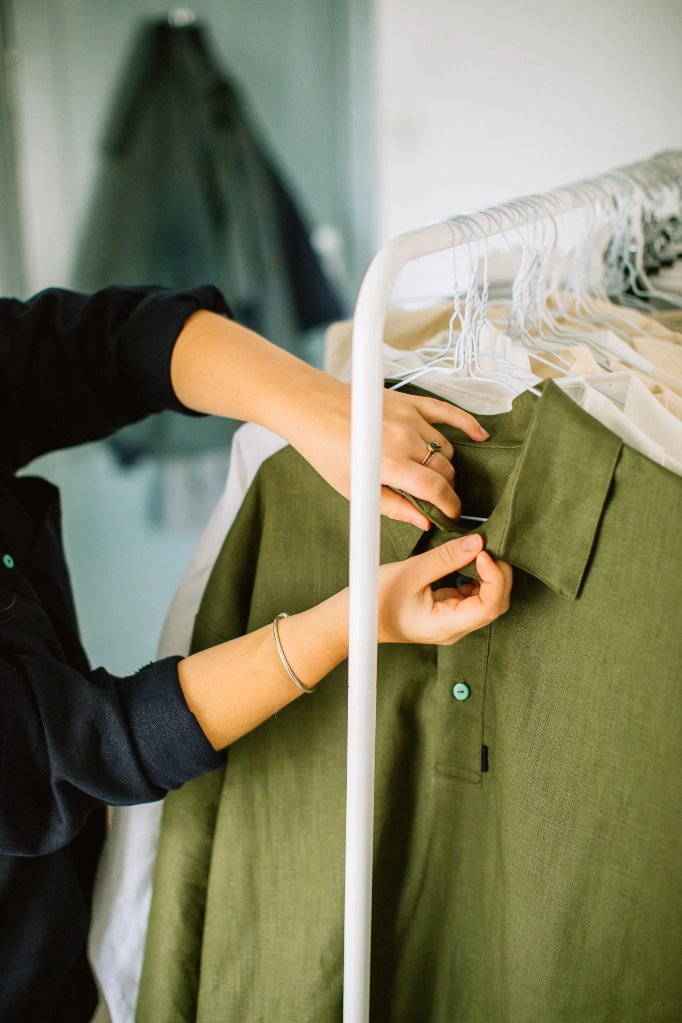 Person's hands adjusting a green shirt on a clothing rack with other white shirts hanging nearby.