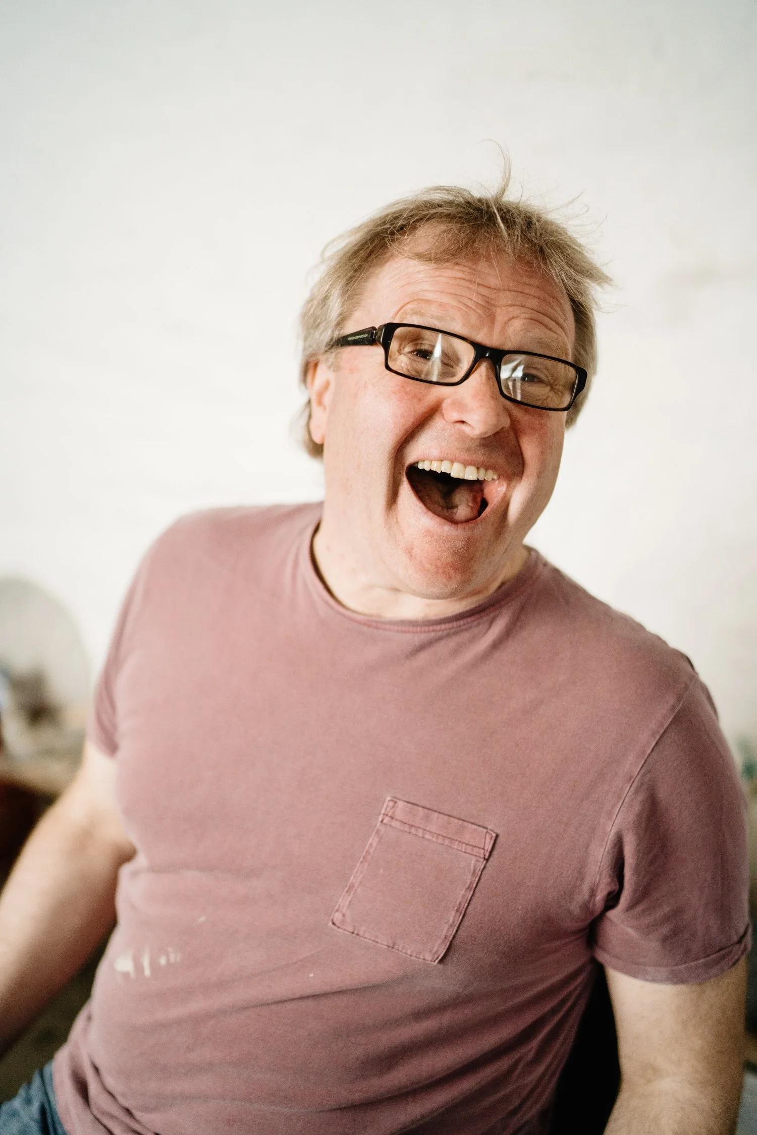 A happy man with glasses, wearing a pink T-shirt, smiling and looking at the camera.