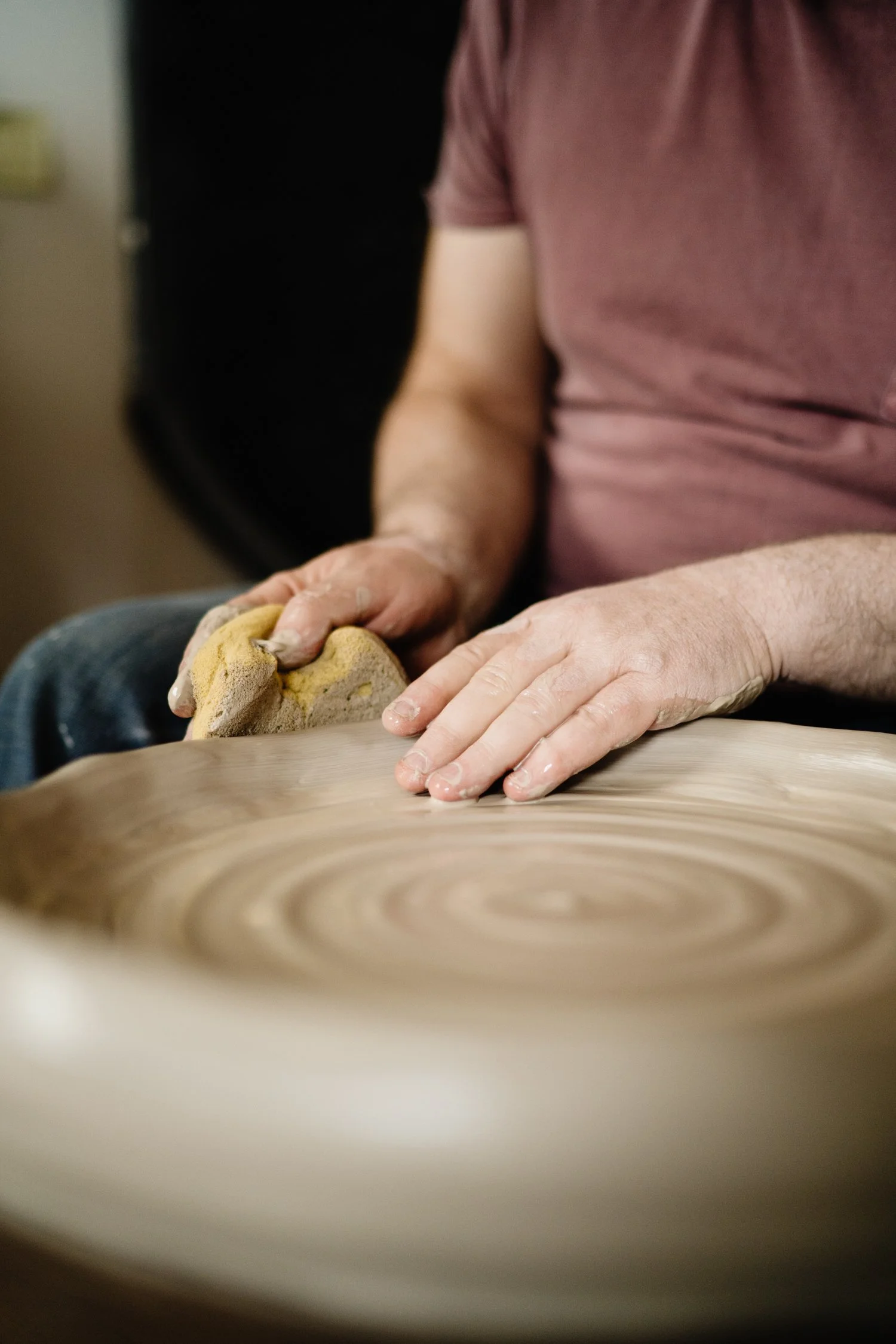 A person shaping clay on a potter's wheel with their hands.