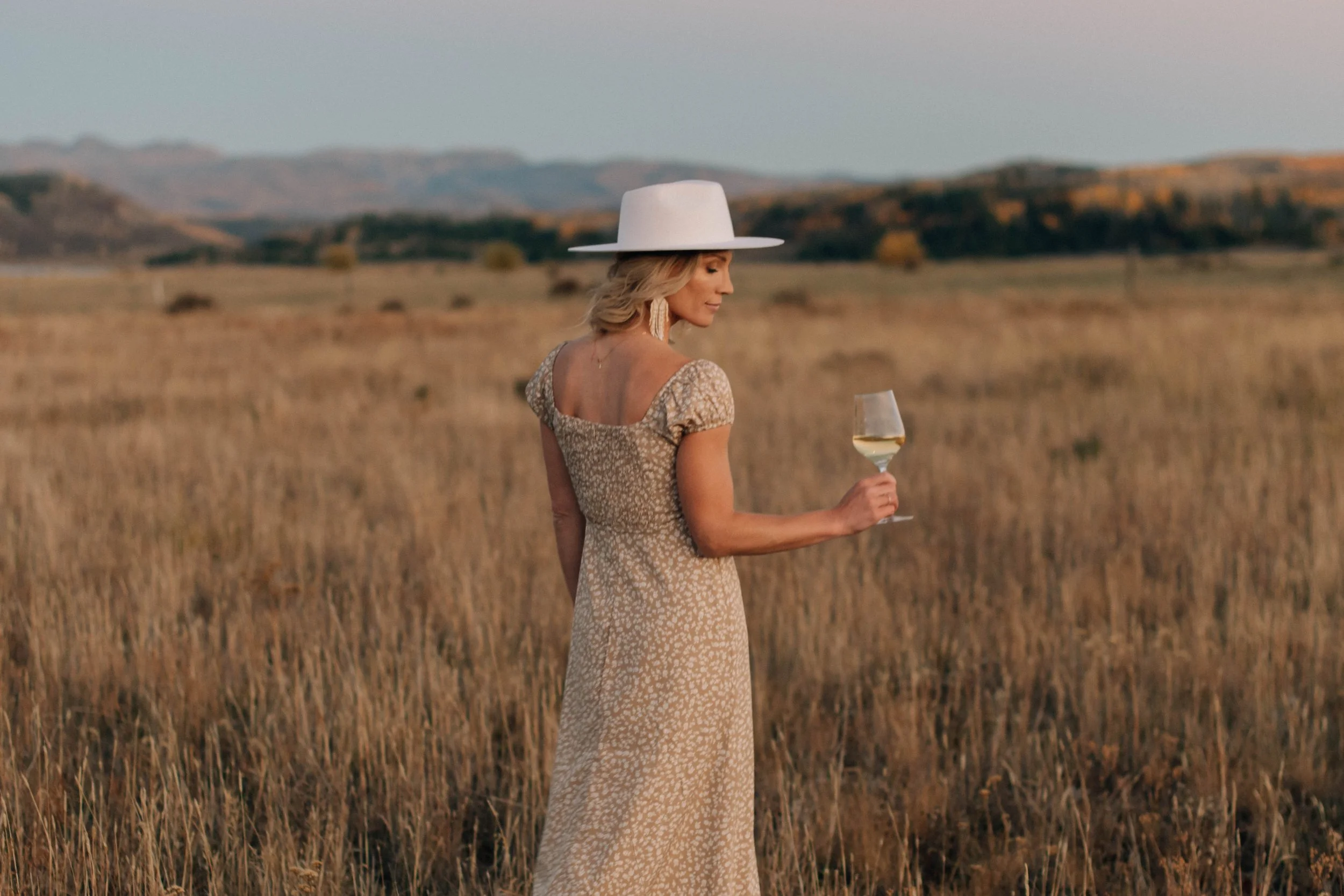 Wine tasting host standing in a field holding a glass of white wine