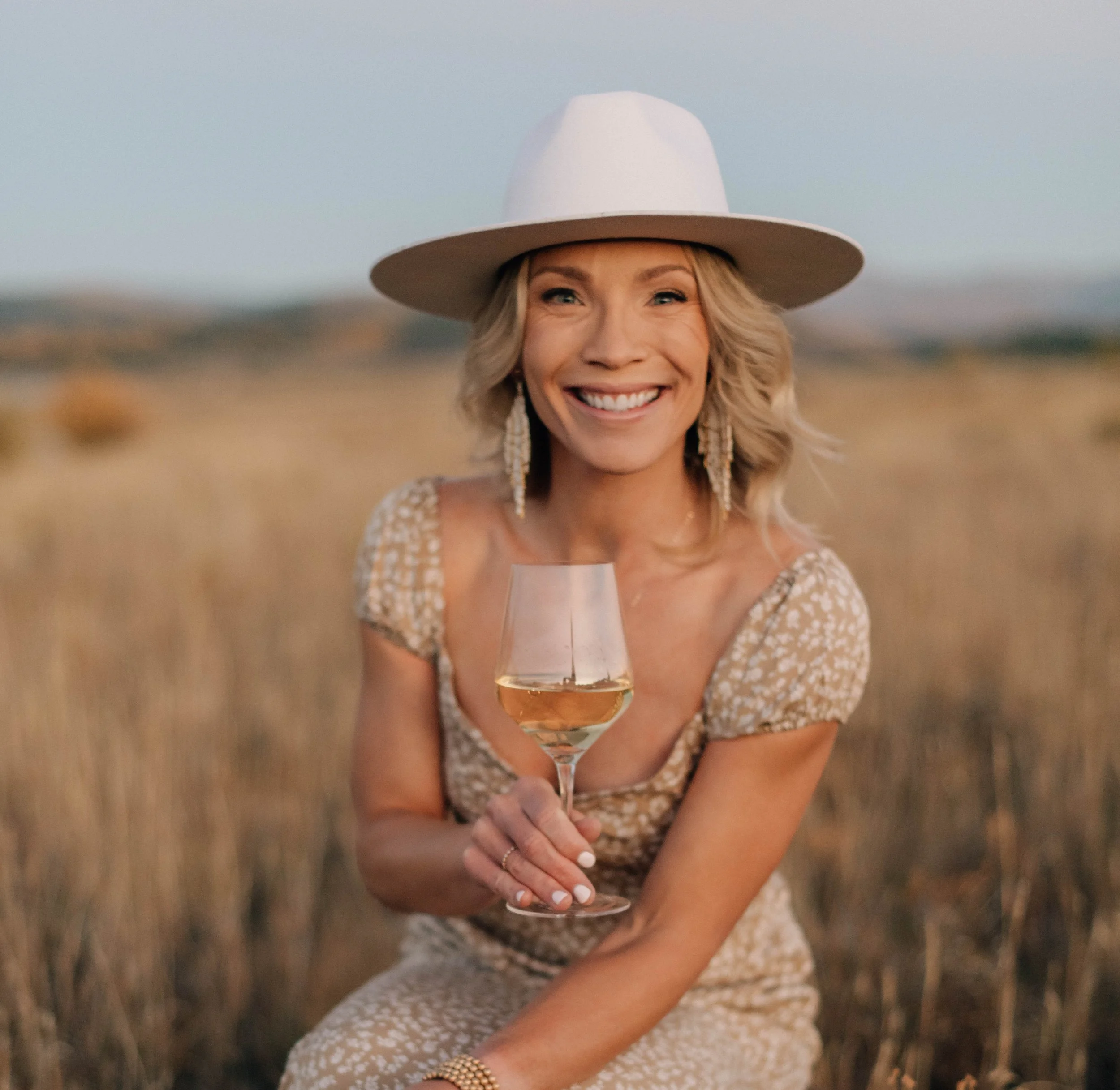 Wine tasting host sitting in a field with a glass of white wine