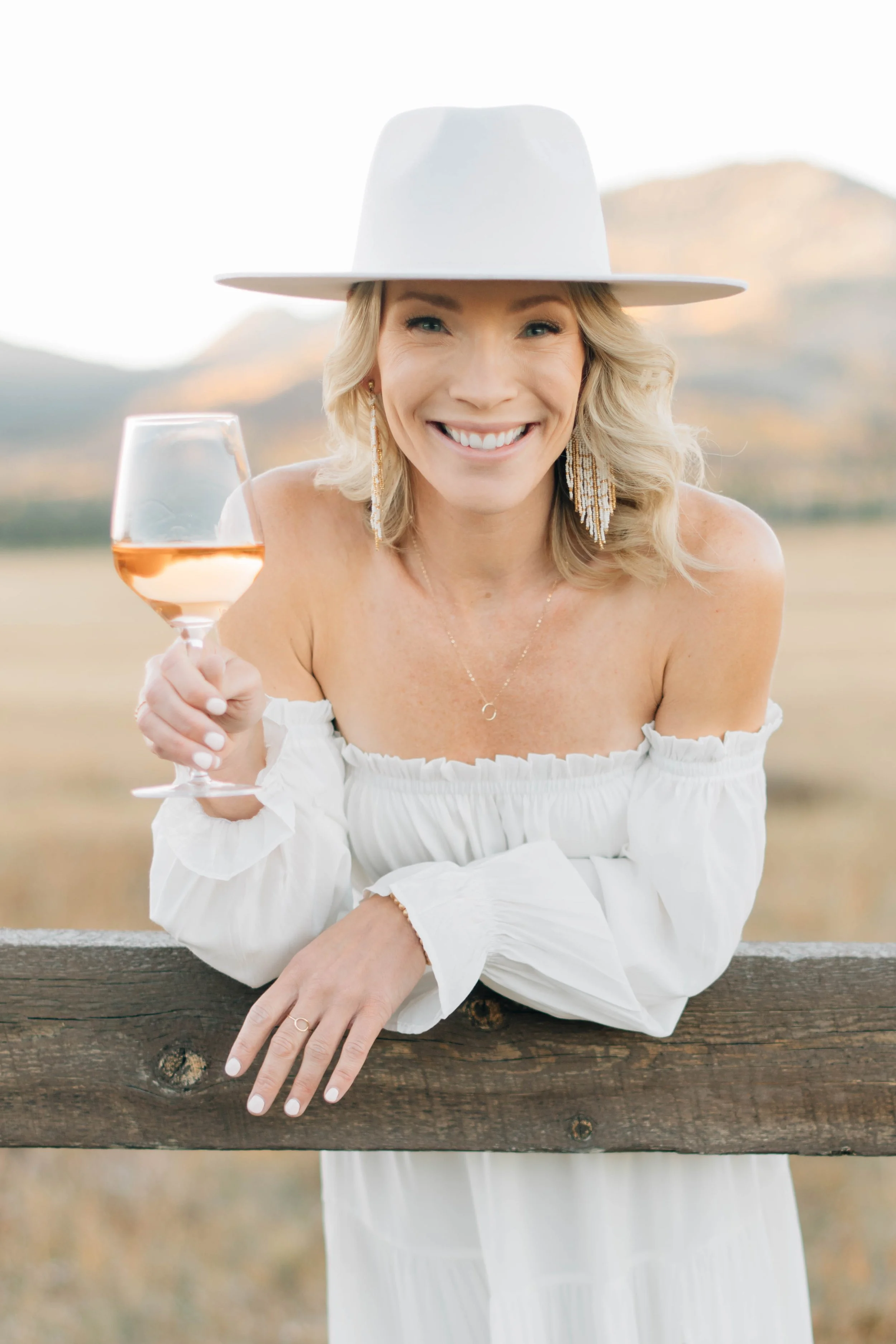 Wine tasting host smiling while holding a glass of rosé and leaning on a wooden fence