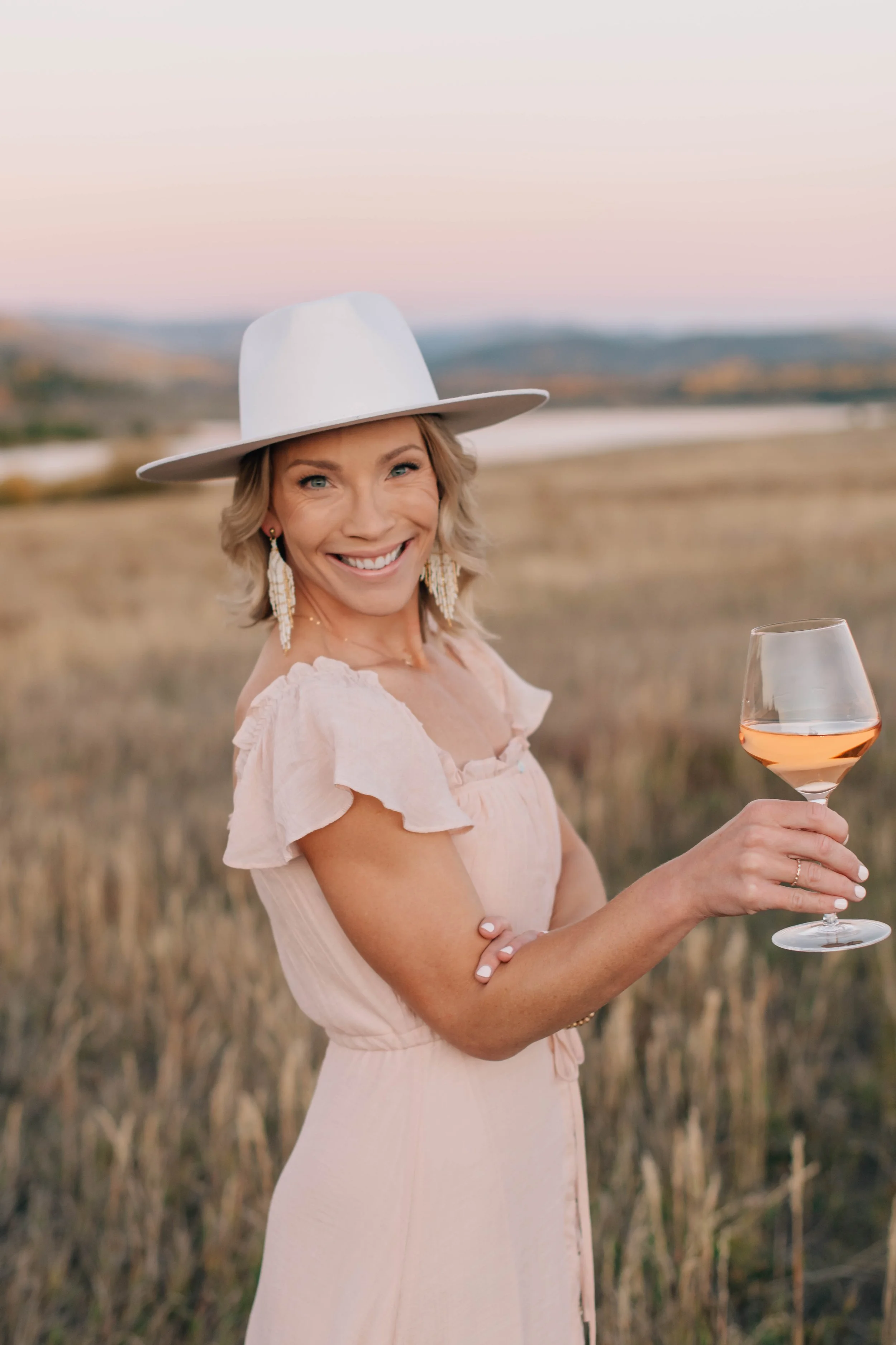 Wine tasting host smiling in profile while holding a glass of rosé in an open field at alpenglow
