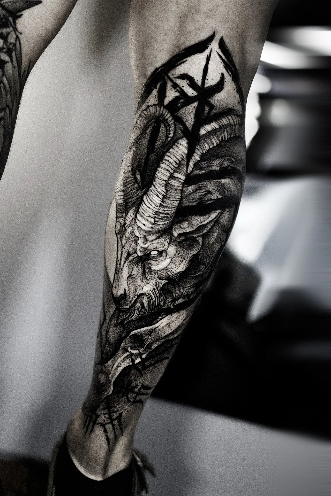 black-and-grey tattoo on a person's calf featuring a majestic ram or goat head