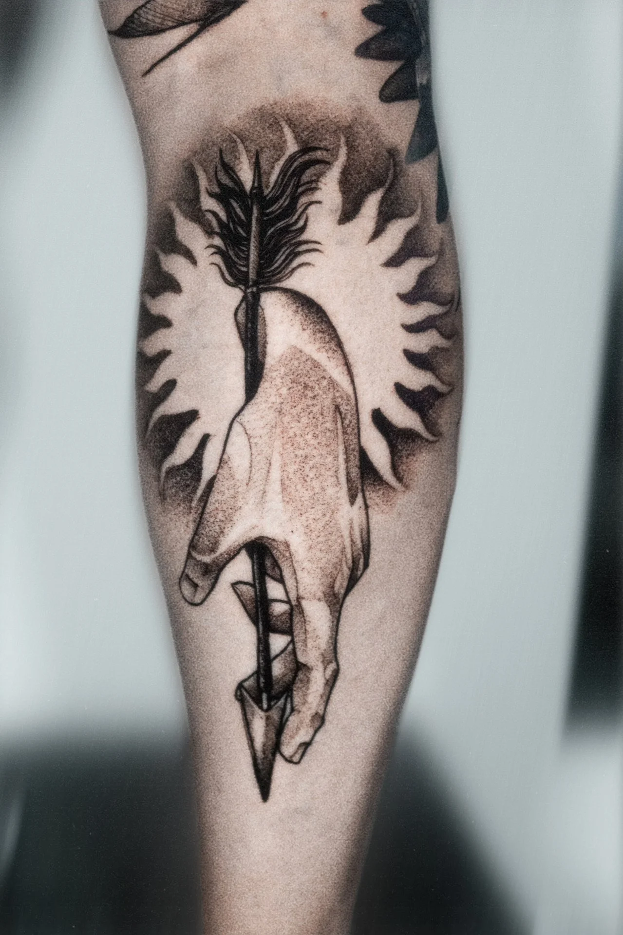 Black-and-gray hand holding dagger tattoo on forearm.