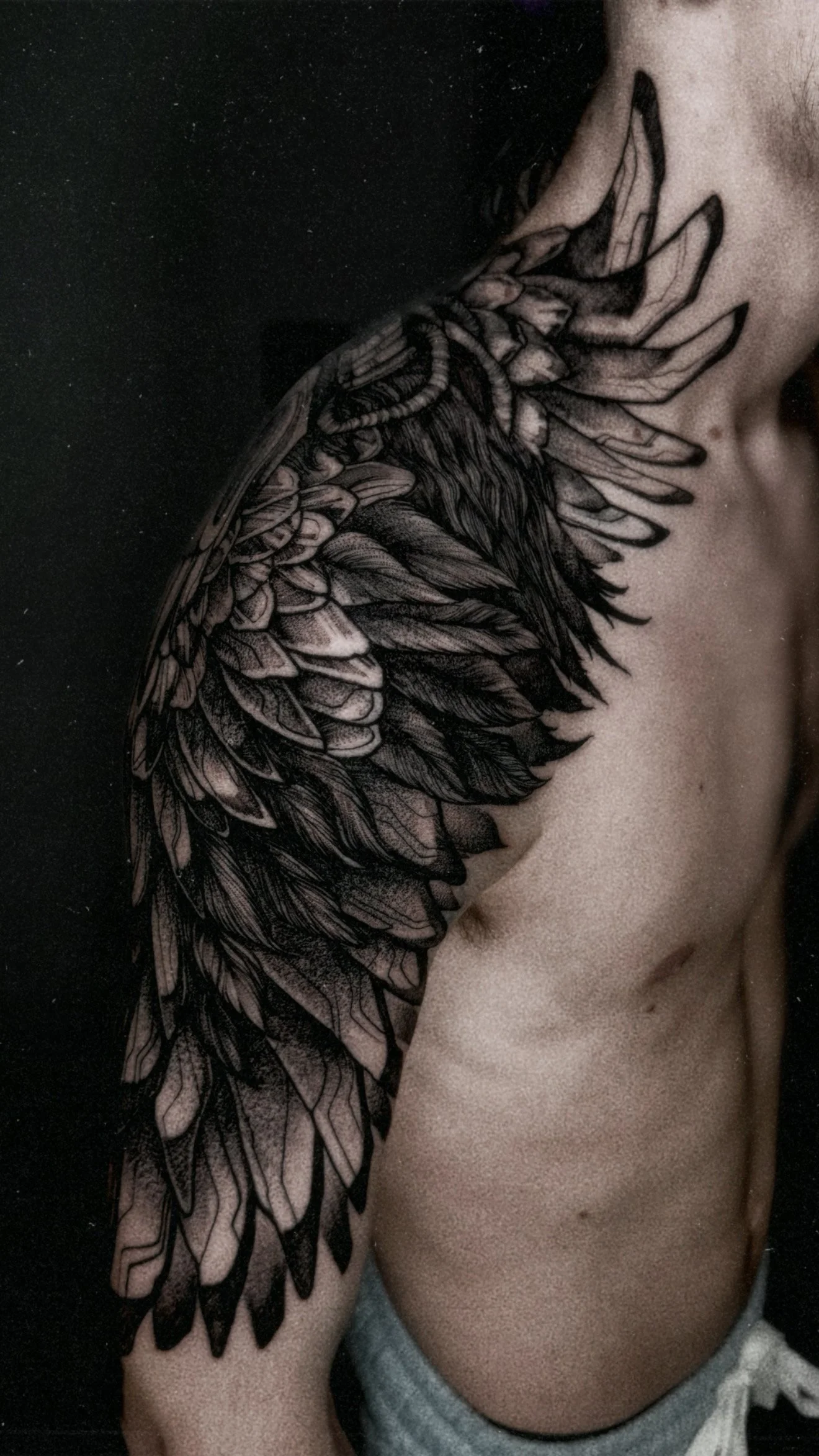 A side profile view of a neck and shoulder tattoo showing the base of a large wing, blending realistic feather textures with mechanical, robotic elements at the "joint."