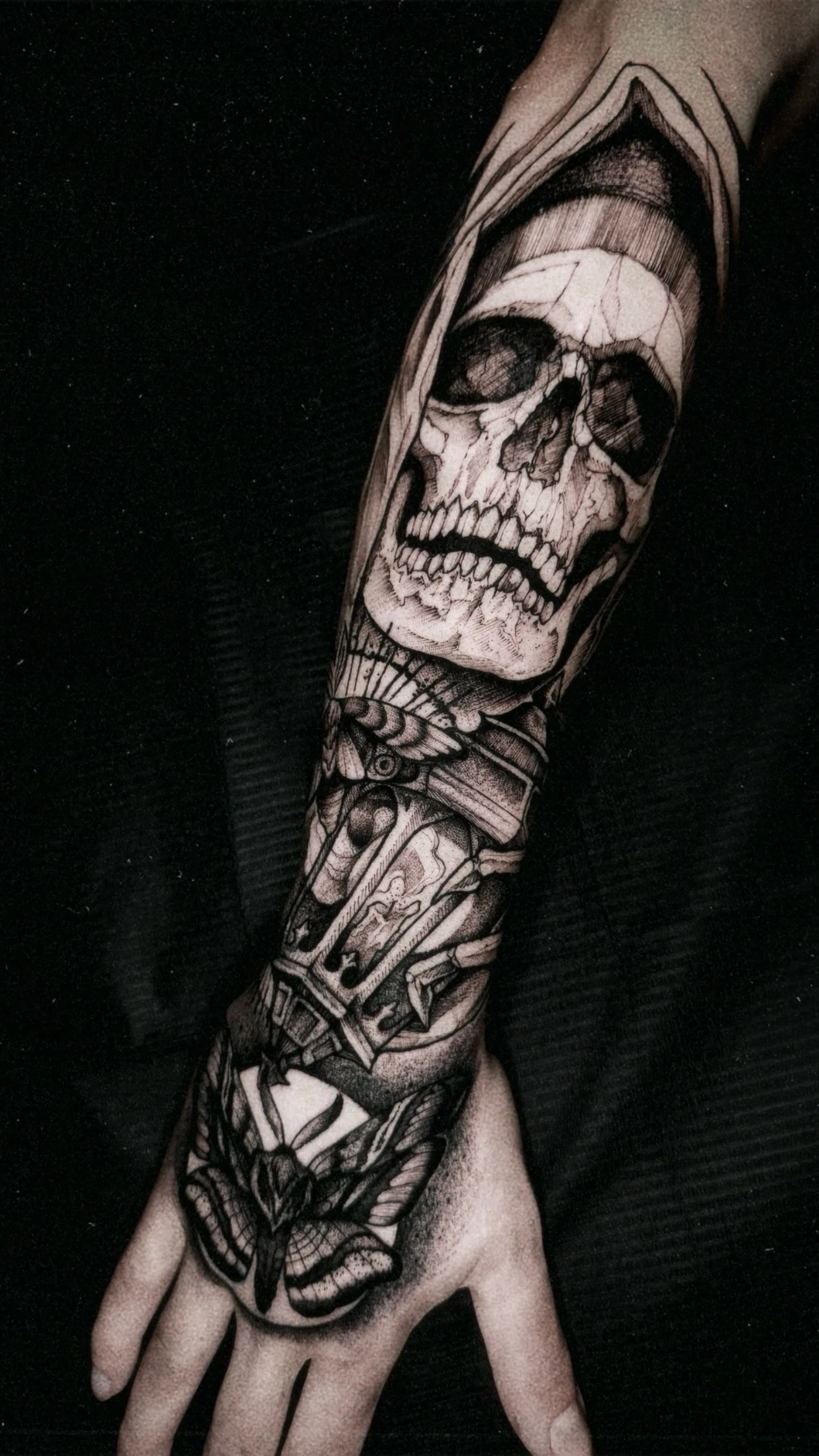 A full-sleeve hand and forearm tattoo featuring a realistic cracked skull wearing a hood, transitioning into a lantern and a moth on the back of the hand.