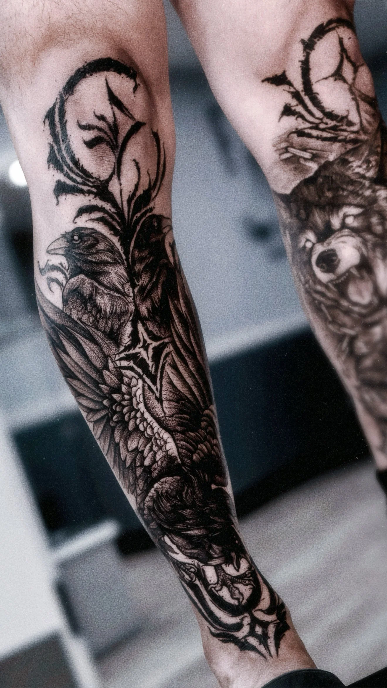 A dark surrealist tattoo on the lower leg featuring a raven and organic, thorny filigree patterns with deep black shading and fine-line detailing.