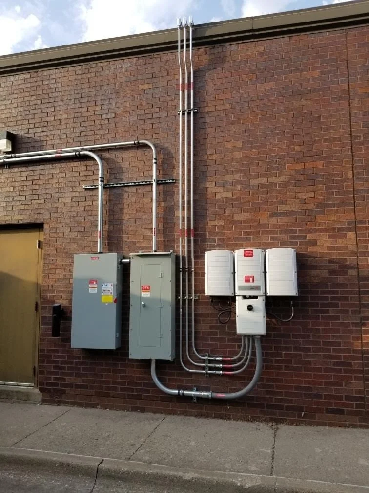 Electrical and utility meters and conduits mounted on a brick wall outside a building.