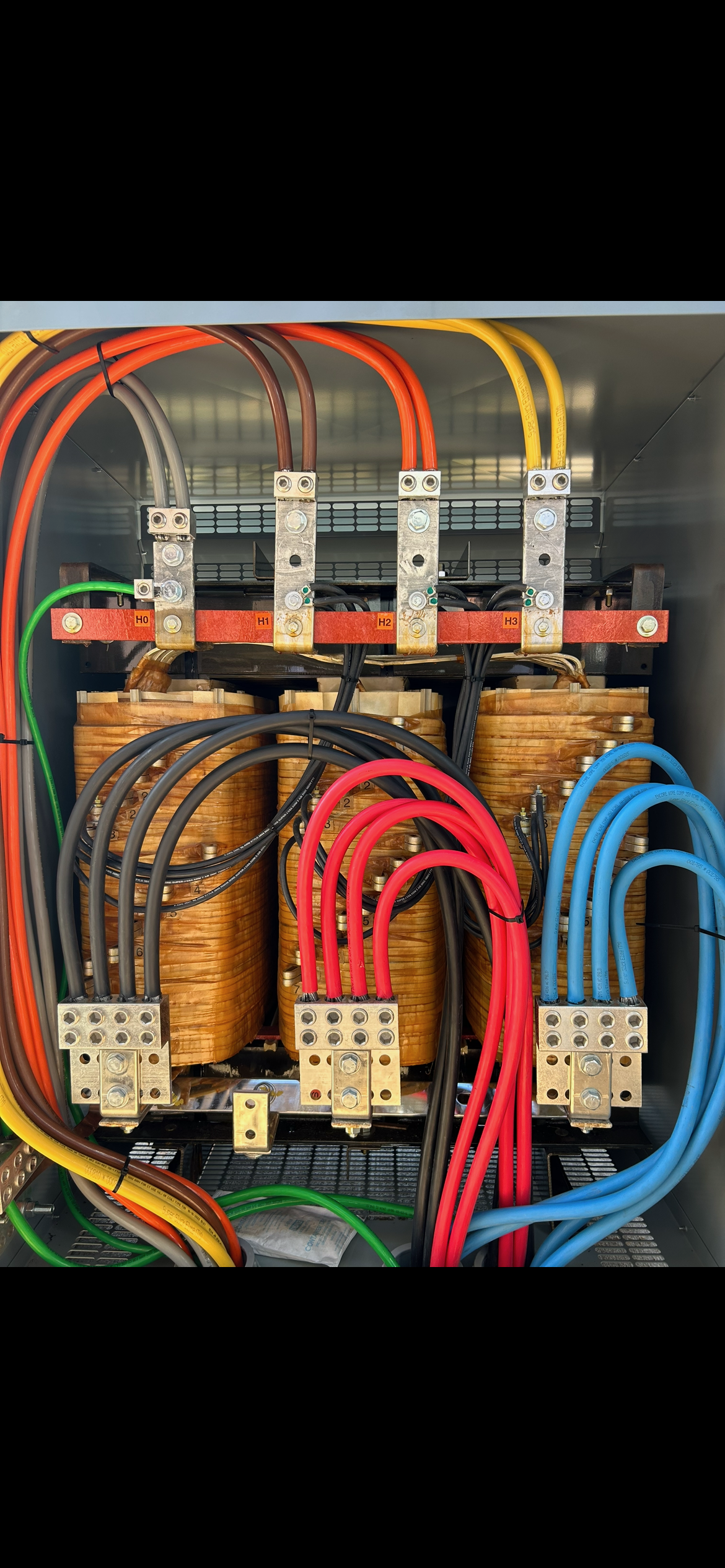 Inside an electrical control panel with colorful wires connected to large transformers and metal terminals.