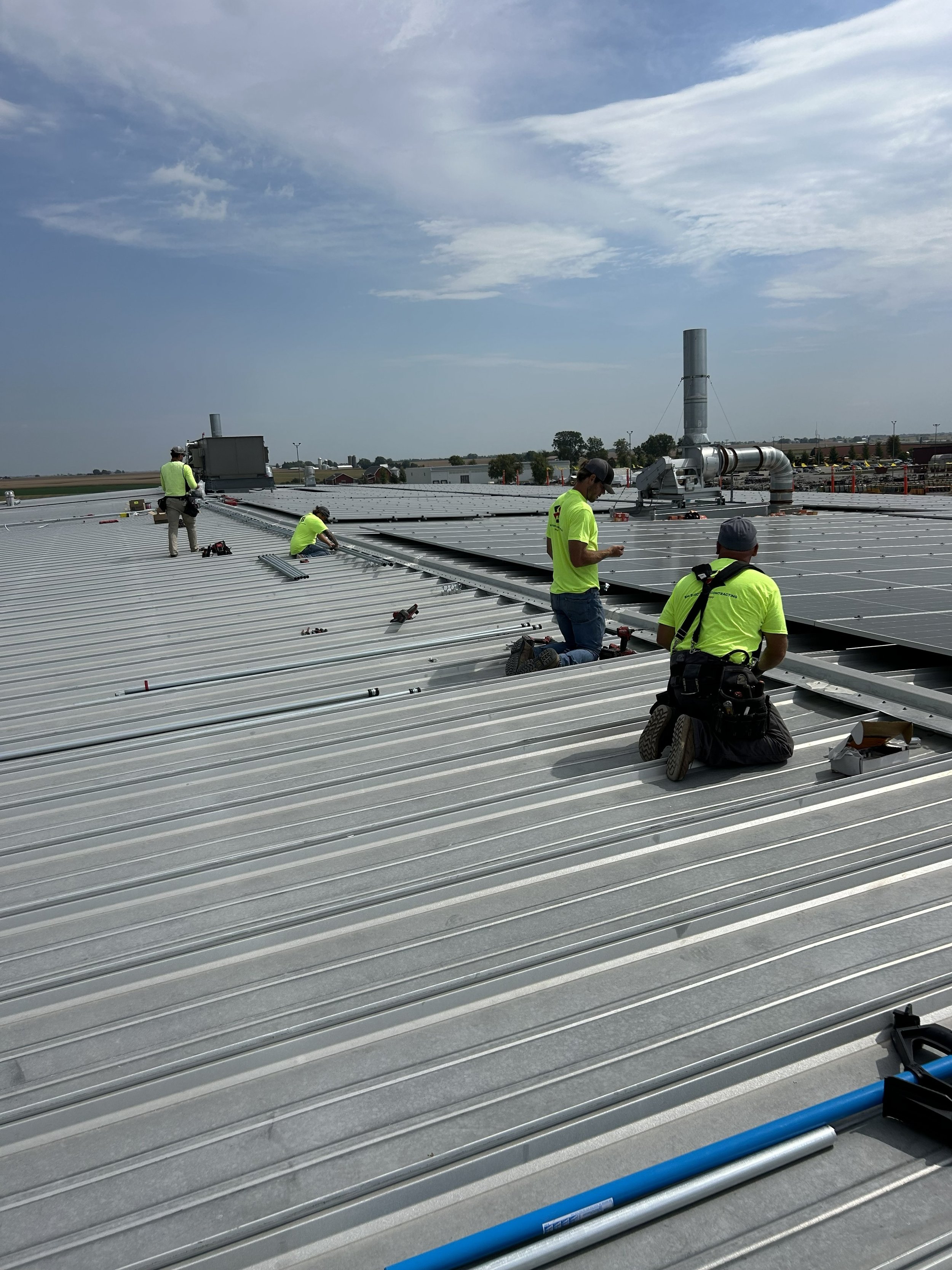 Workers installing solar panels on a rooftop under a cloudy sky.