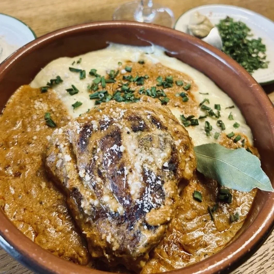 Plat de viande avec sauce, accompagné de purée et garnitures, servi dans un bol en terre cuite.