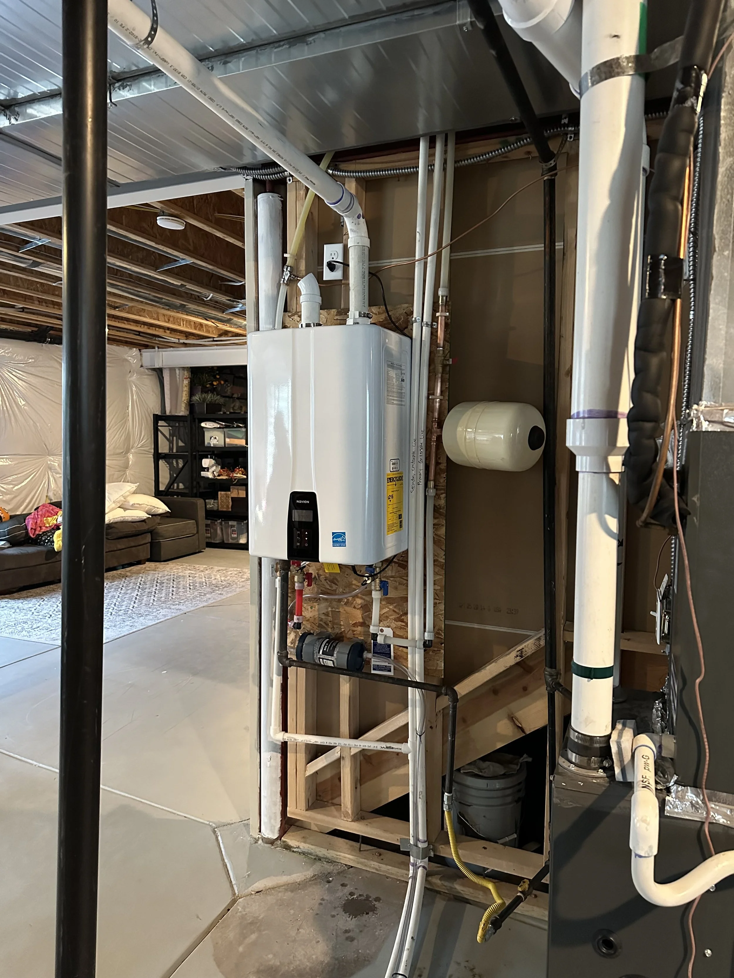 Furnace or water heater installation in a basement with plumbing pipes and construction framing visible.