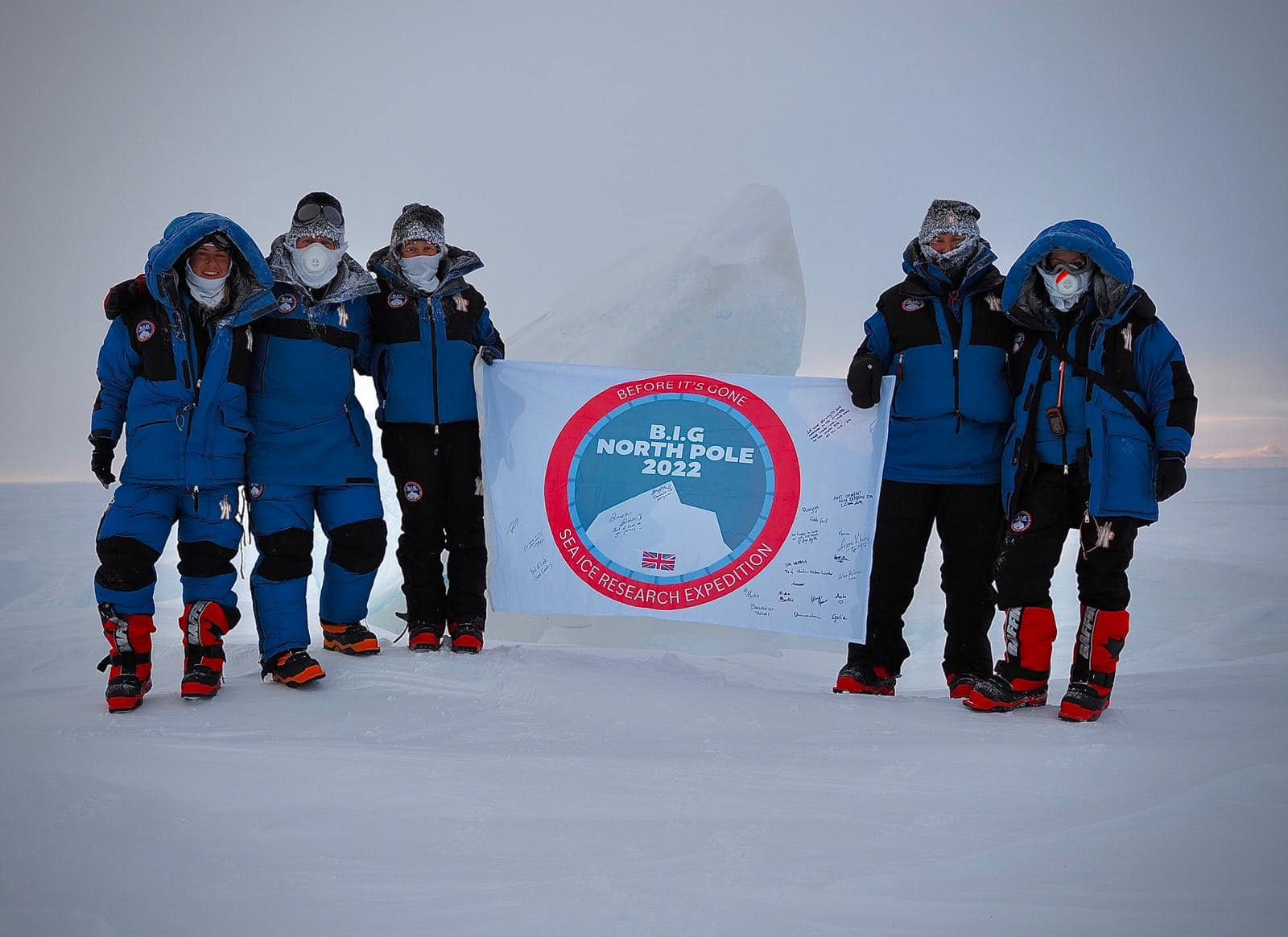 Group of six people in winter gear holding a banner at the North Pole, with a snow and ice background, celebrating the 2022 SEA ICE RESEARCH EXPEDITION.