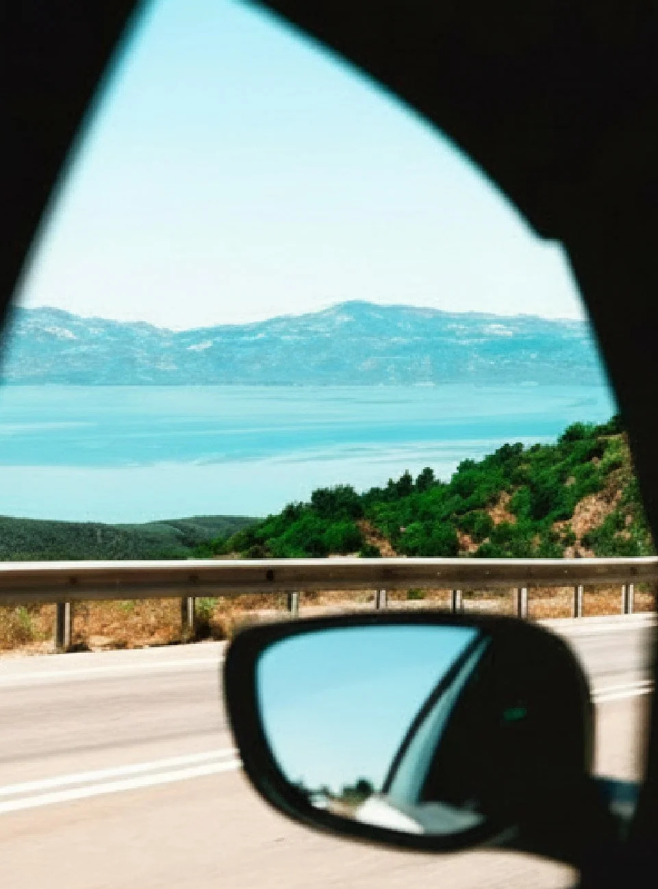 Driving along the Croatian coast with a view of the sea and islands reflected in a car side mirror.