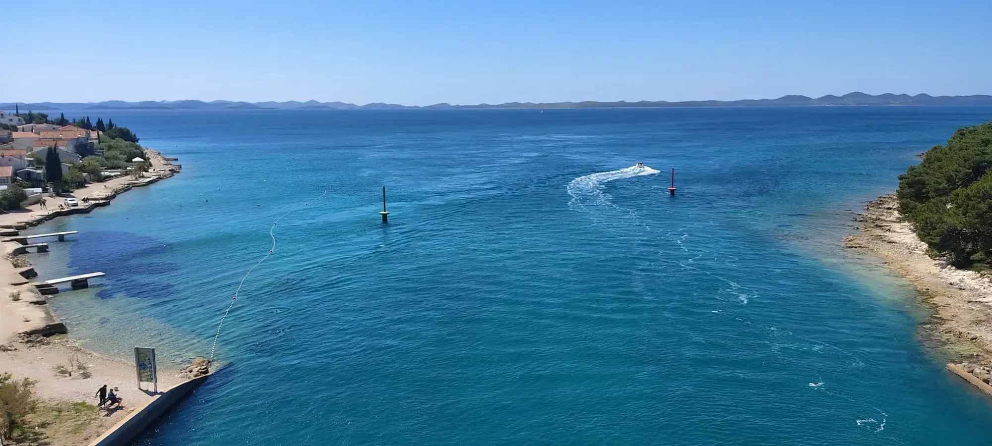 Panoramic view from Ždrelac bridge showing turquoise sea, coastal paths, and two lighthouses between Ugljan and Pasman islands.