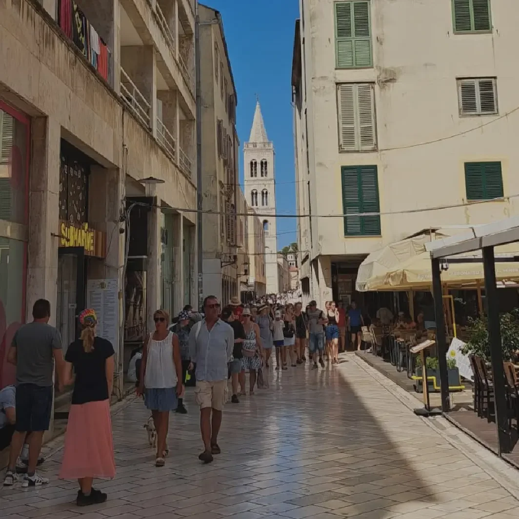A charming street scene in Zadar Old Town with people walking past authentic local boutiques and artisan shops.
