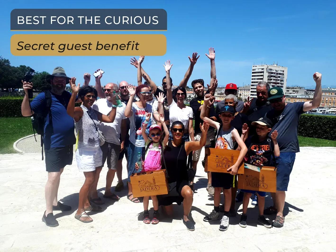 A large, happy group of families and friends holding wooden suitcases and cheering in Zadar's Old Town during the Jadera Secrets outdoor escape game adventure.