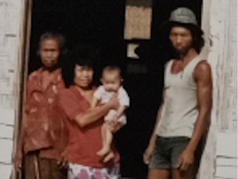 Family standing in front of an old building, a man on the right, and two ladies on the left  one holding a baby.